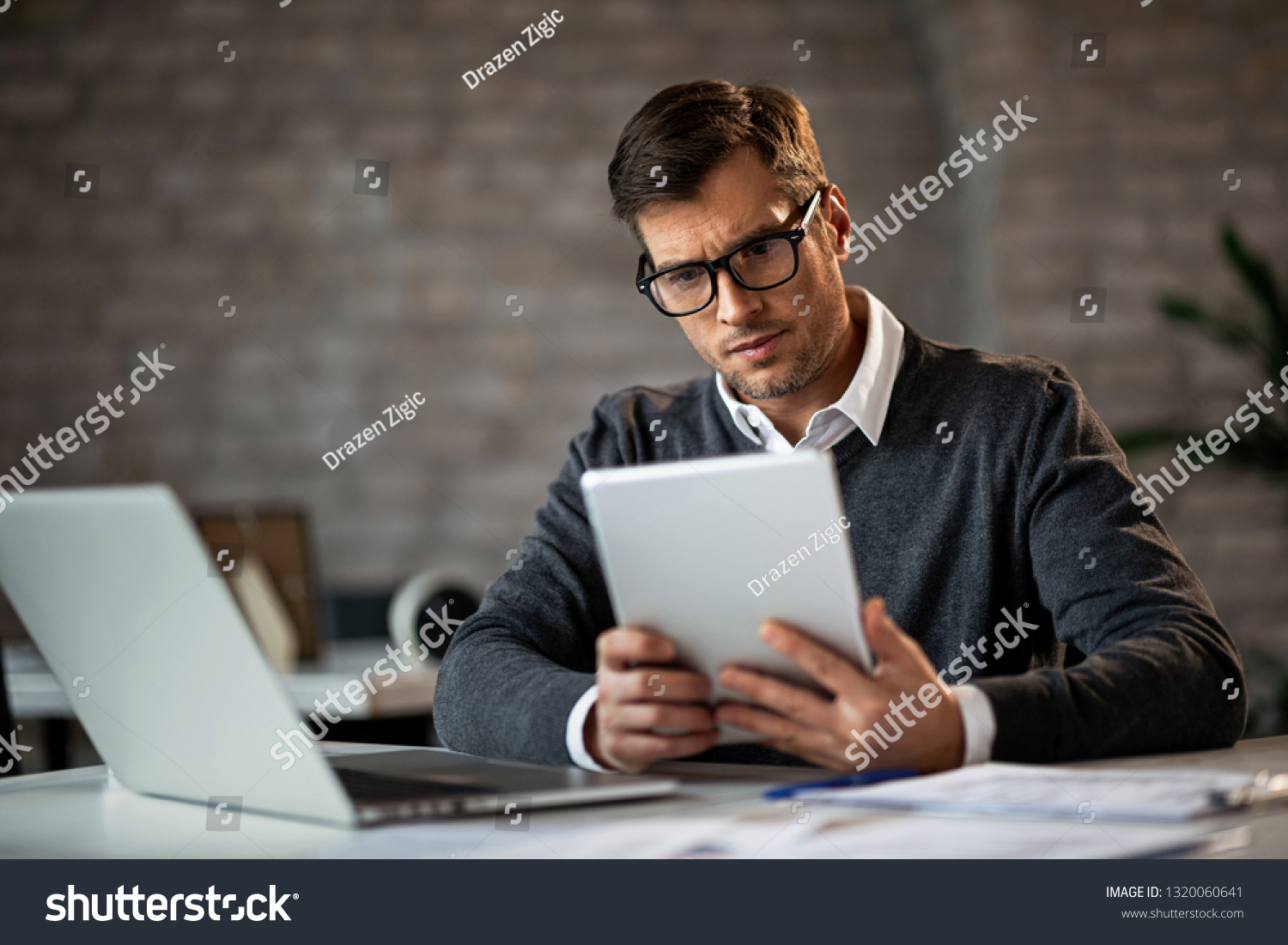 Mid adult entrepreneur working at his office desk and using digital tablet.  #1320060641
