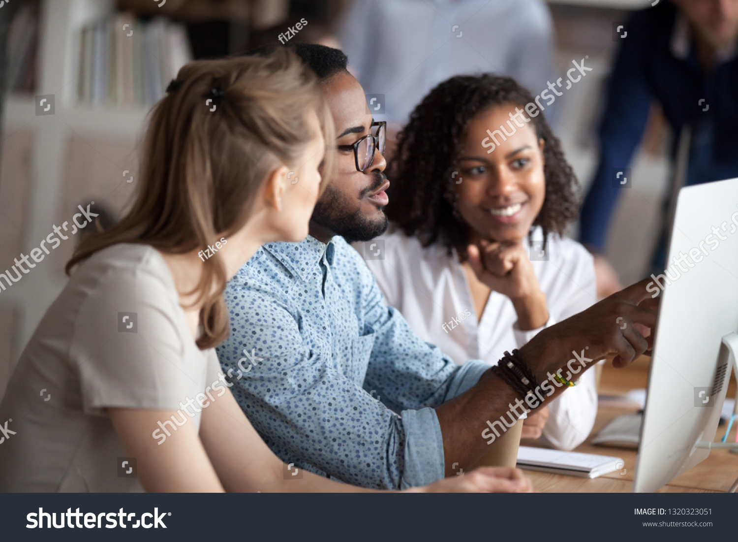 Diverse businesspeople working in shared office, focus on black american team leader sitting at desk together with females colleagues, mentor helps understand research data company corporate program #1320323051