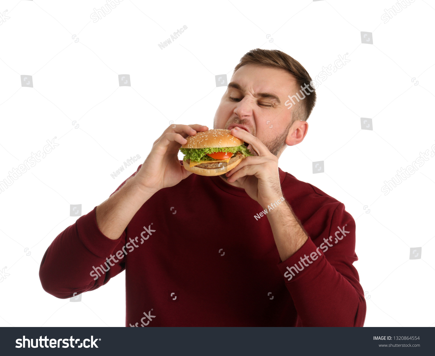 Young man eating tasty burger on white background #1320864554