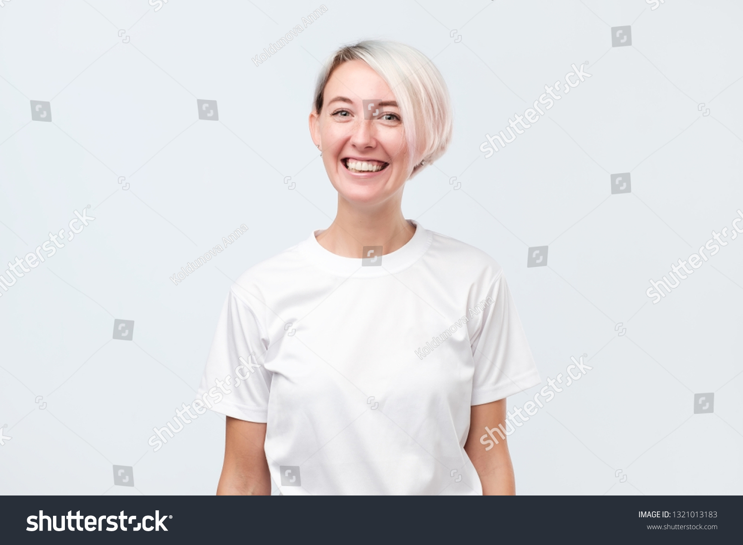 Attractive woman in white t-shirt with short dyed hair being very glad smiling with broad smile showing her perfect teeth having fun indoors. #1321013183