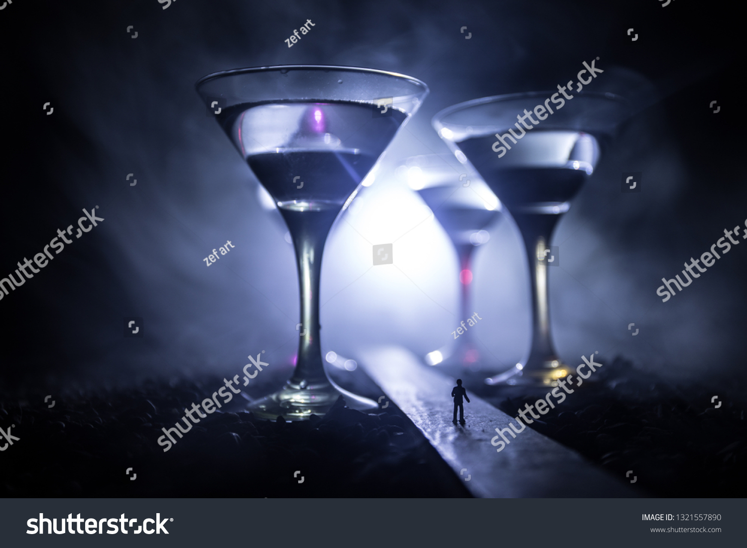 Abstract alcoholism concept. Silhouette of a man standing in the middle of the road on a misty night with giant glasses filled with alcoholic beverage. Creative artwork decoration #1321557890