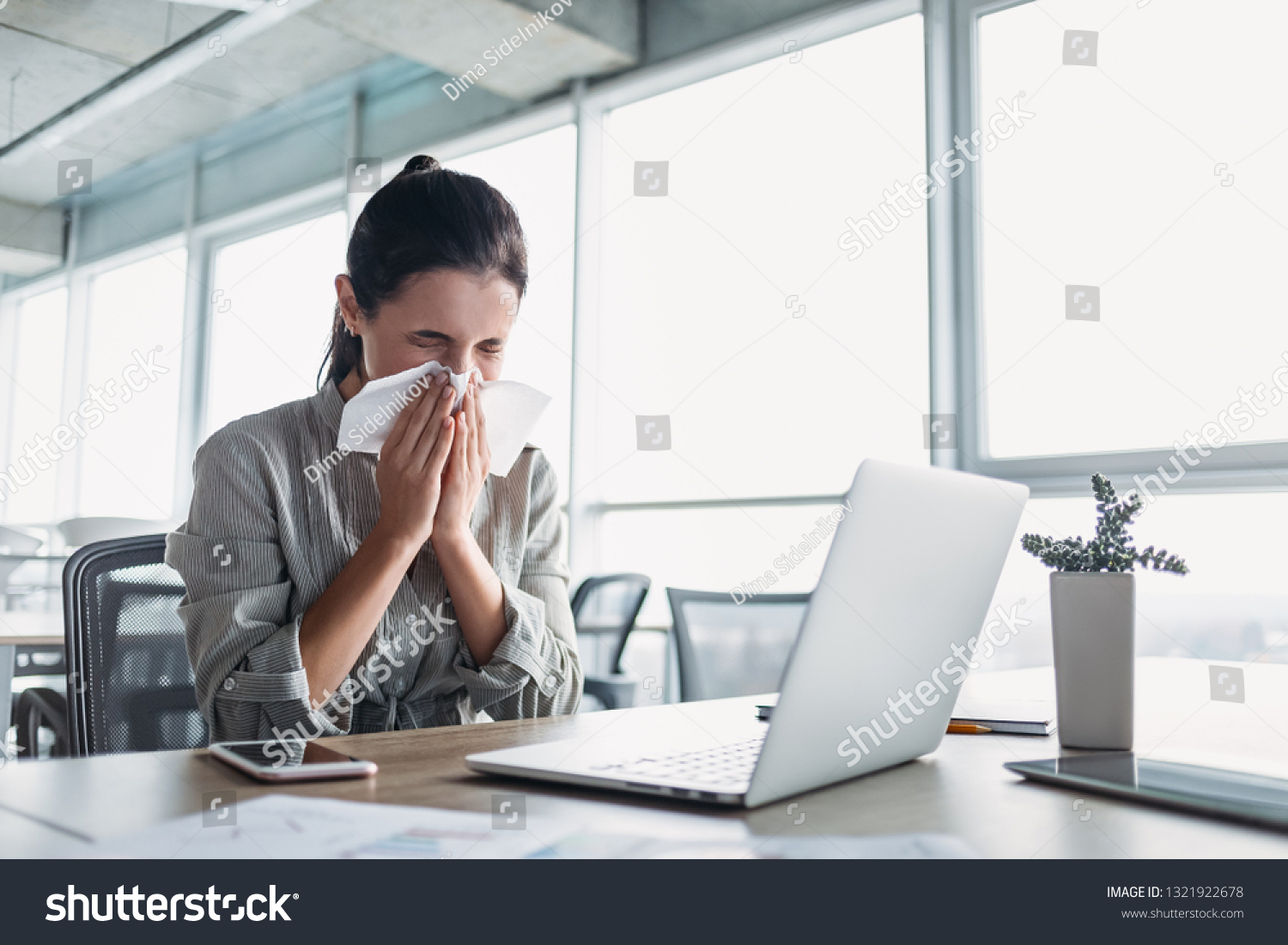 Sick and overworked businesswoman sitting at the desk in the office and blowing her nose, feeling unwell. #1321922678