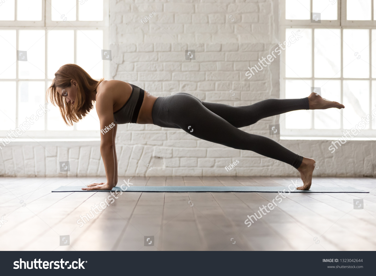 Sporty woman in grey sportswear, bra and leggings practicing yoga, doing Push ups or press ups exercise, phalankasana, variation of Plank pose, beautiful girl working out at home or in yoga studio #1323042644