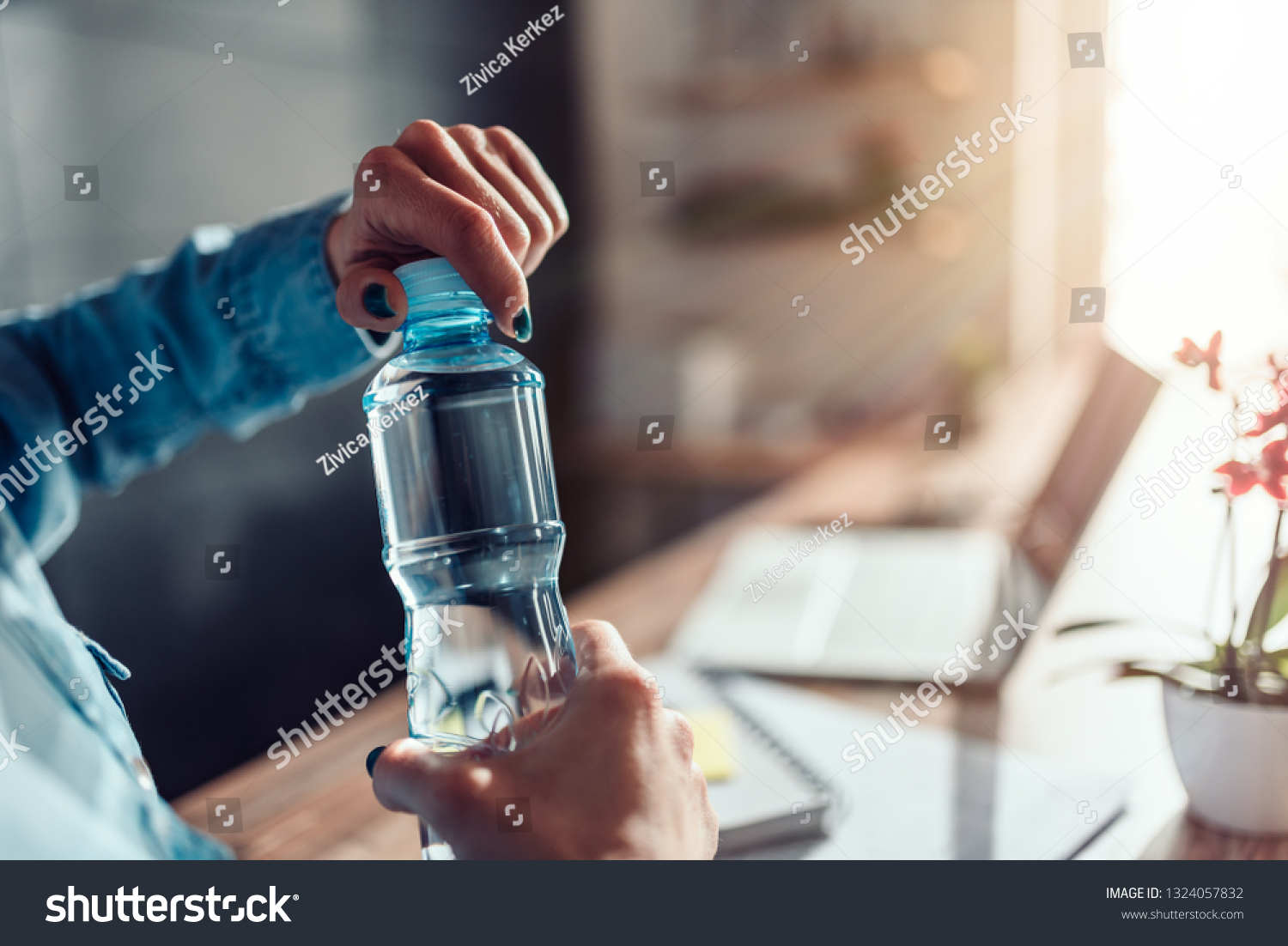 Woman wearing denim shirt working in the office and opening plastic bottle of water #1324057832