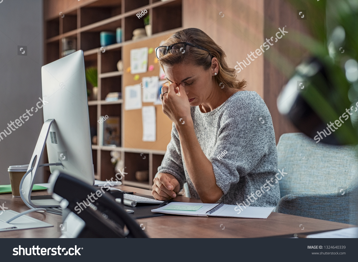 Exhausted businesswoman having a headache at office. Mature creative woman working at office desk feeling tired. Stressed casual business woman feeling eye pain while overworking on desktop computer. #1324640339