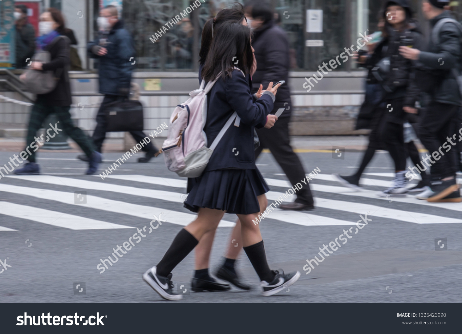 TOKYO, JAPAN - FEBRUARY 27TH, 2019. Japanese school girls crossing the famous Shibuya scramble crosswalk in winter. #1325423990