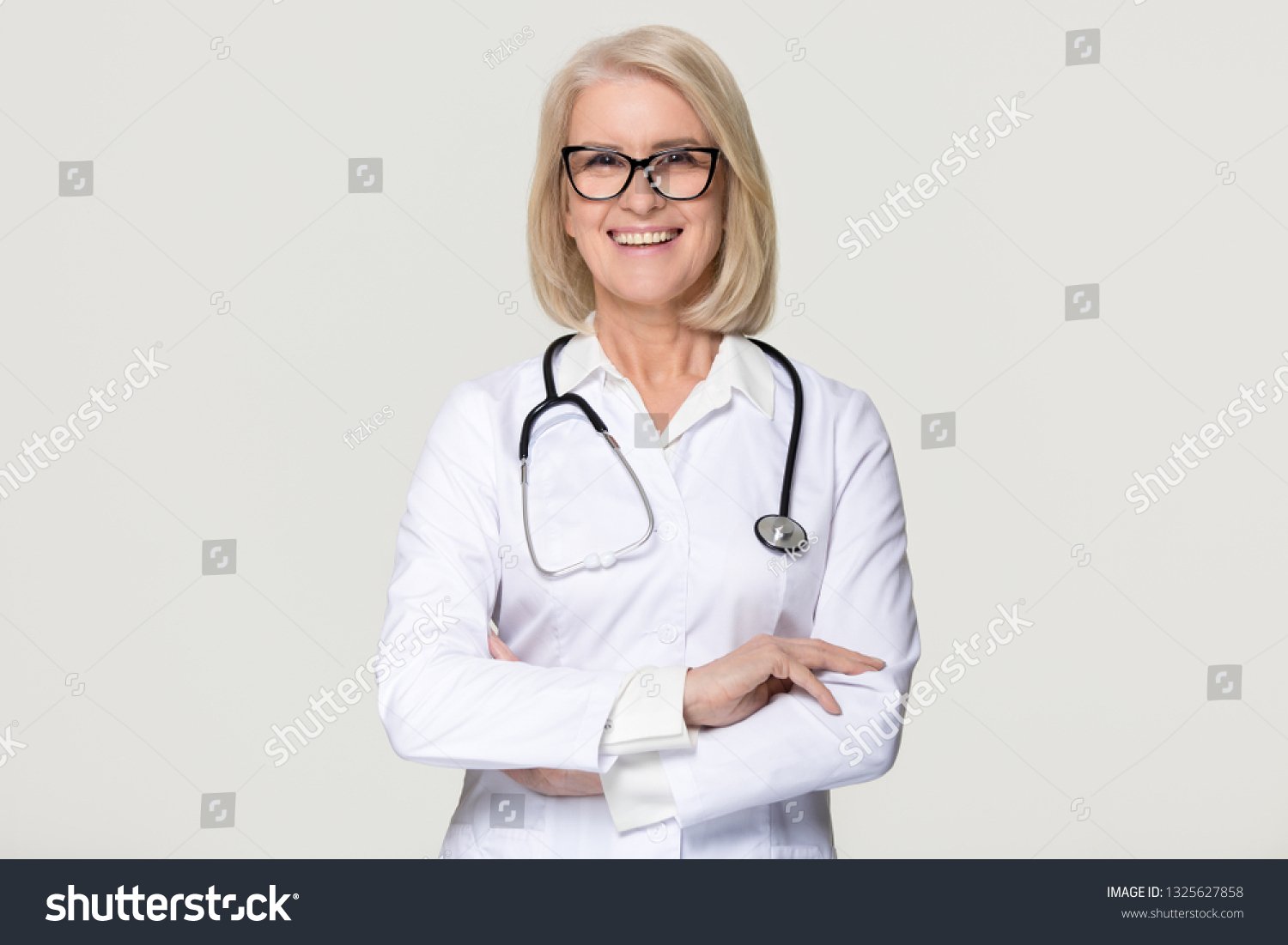 Happy mature middle aged woman doctor medical nurse portrait, smiling old senior female physician practitioner in uniform with stethoscope isolated on white grey studio background, healthcare concept #1325627858