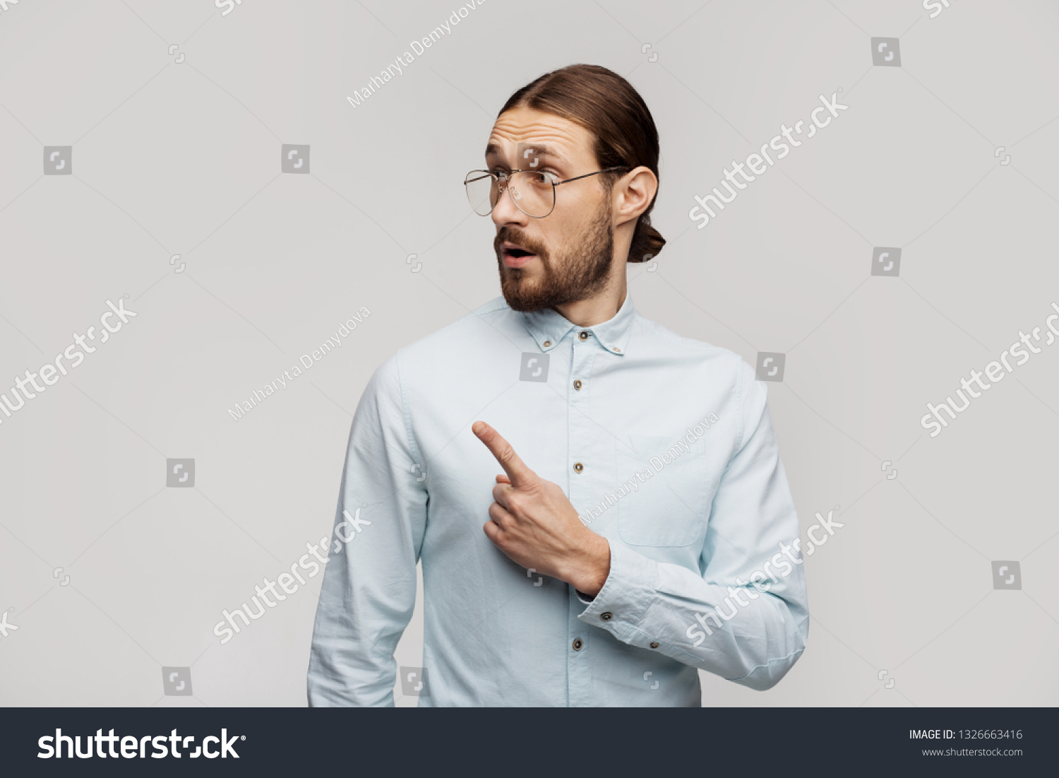 Look here left! Use this image for your website. Man pointing over grey studio background wall on copyspace for some information, advertising, logo. Lifestyle, emotional freestyle. Emotive feelings #1326663416