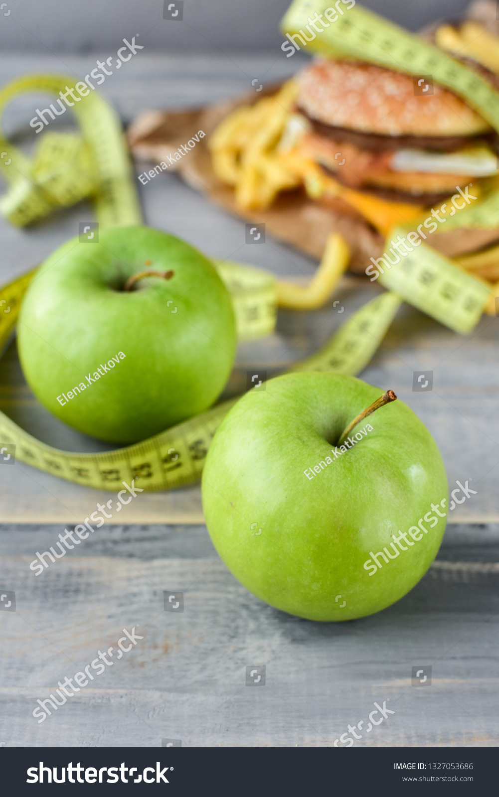 green apples on the background of a burger and fries. Sewing Tape Measures on the food. concept of opposition  healthy food and junk food. selective focus #1327053686