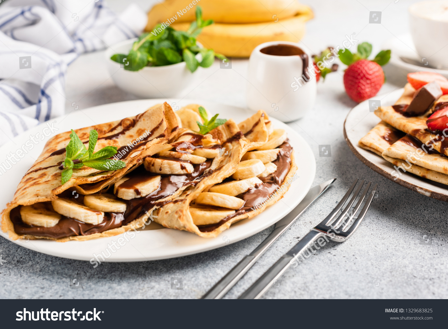 Chocolate hazelnut spread and banana filled crepes on plate. Tasty crepes or blini with sweet sauce and fruits. Closeup view #1329683825