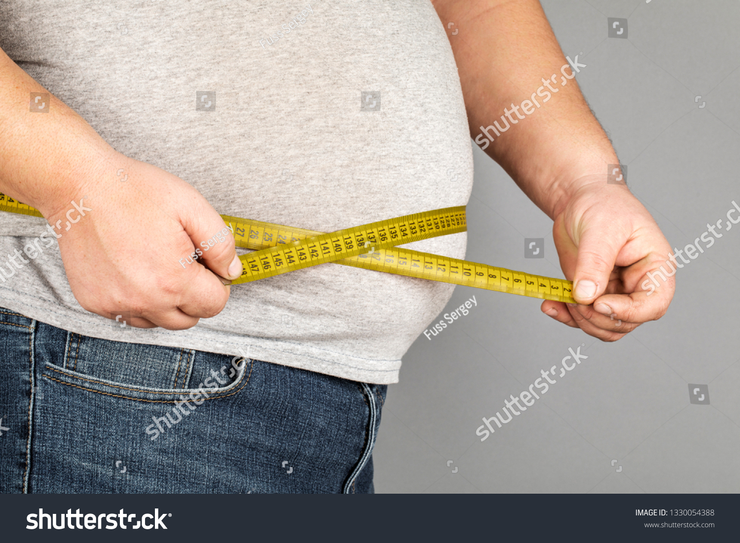 A man measures his fat belly with a measuring tape. on a gray background #1330054388