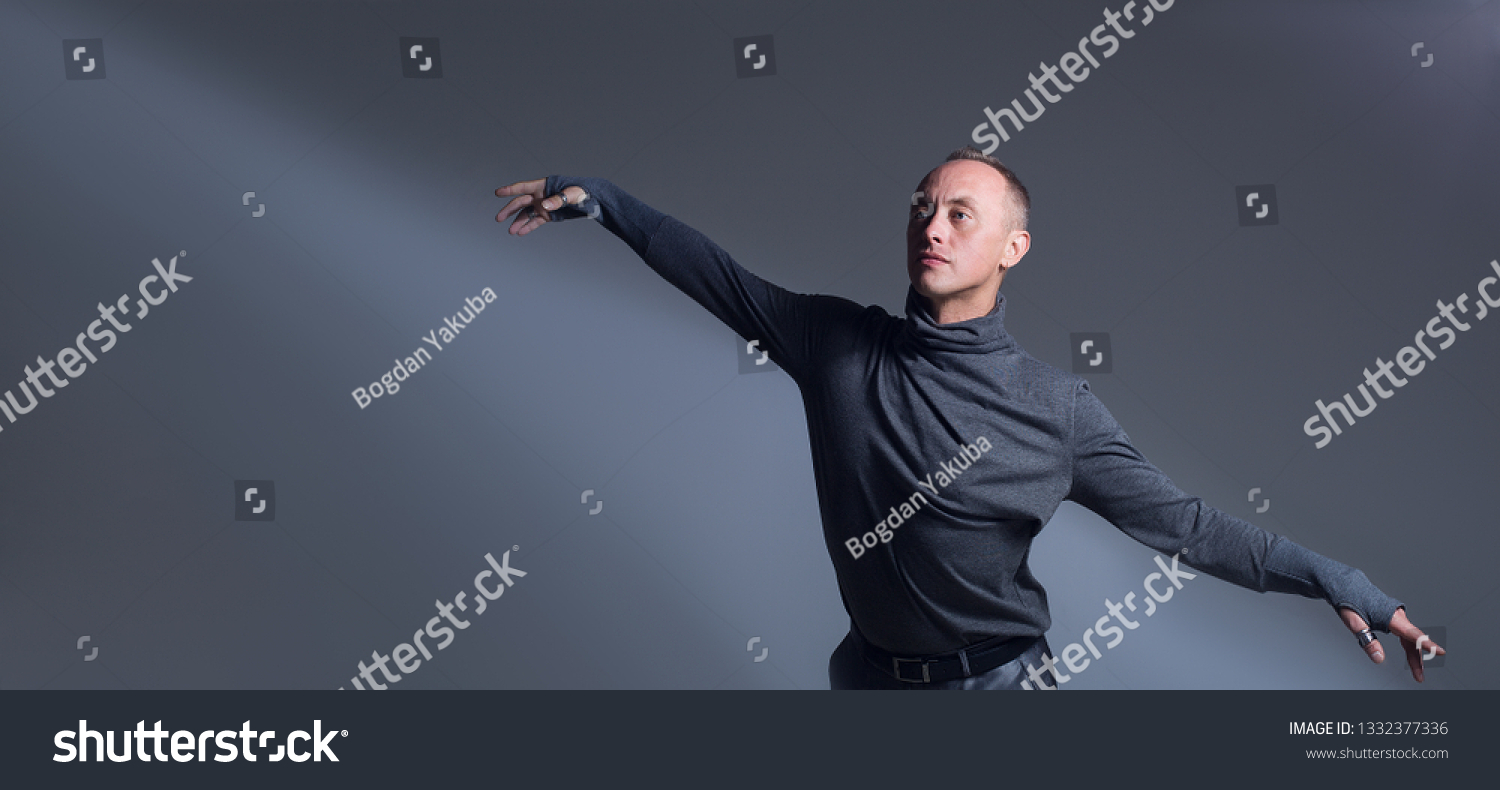 The guy is dancing Contemporary in a gray turtleneck. The man opens his arms like wings and this is underlined by a shadow pattern on a gray background. The ease and grace of dance. #1332377336