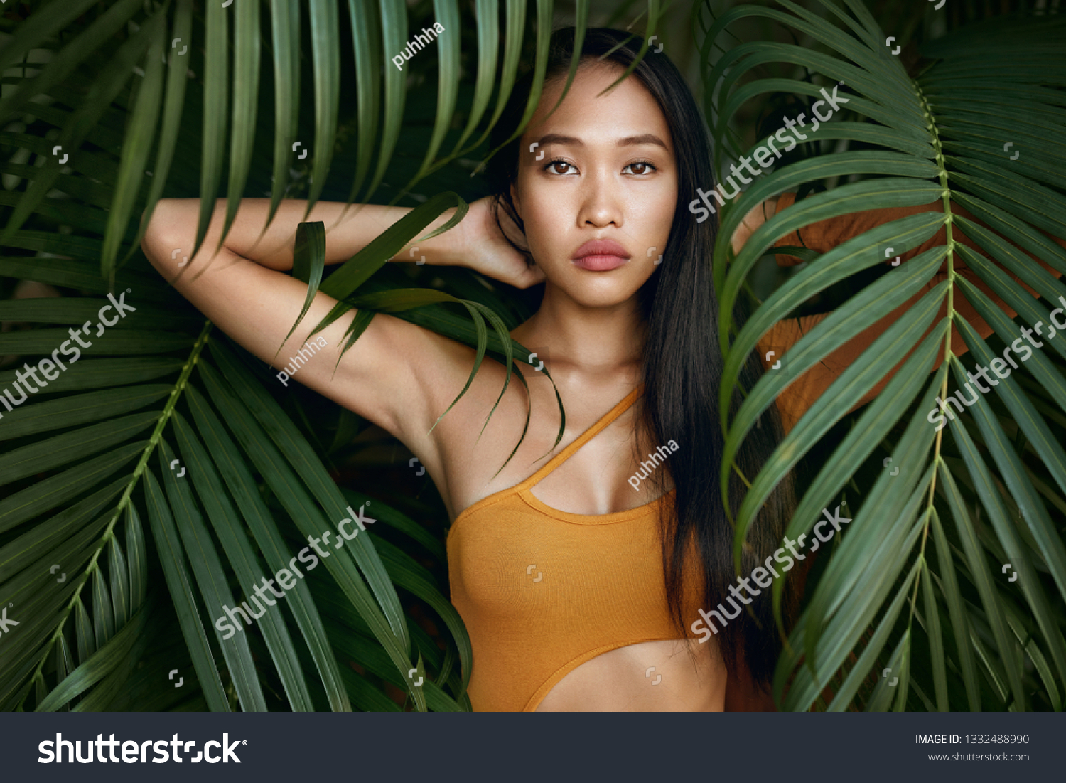 Beauty. Woman model with long straight hair and palm leaves. Asian girl with beautiful exotic face at tropical nature