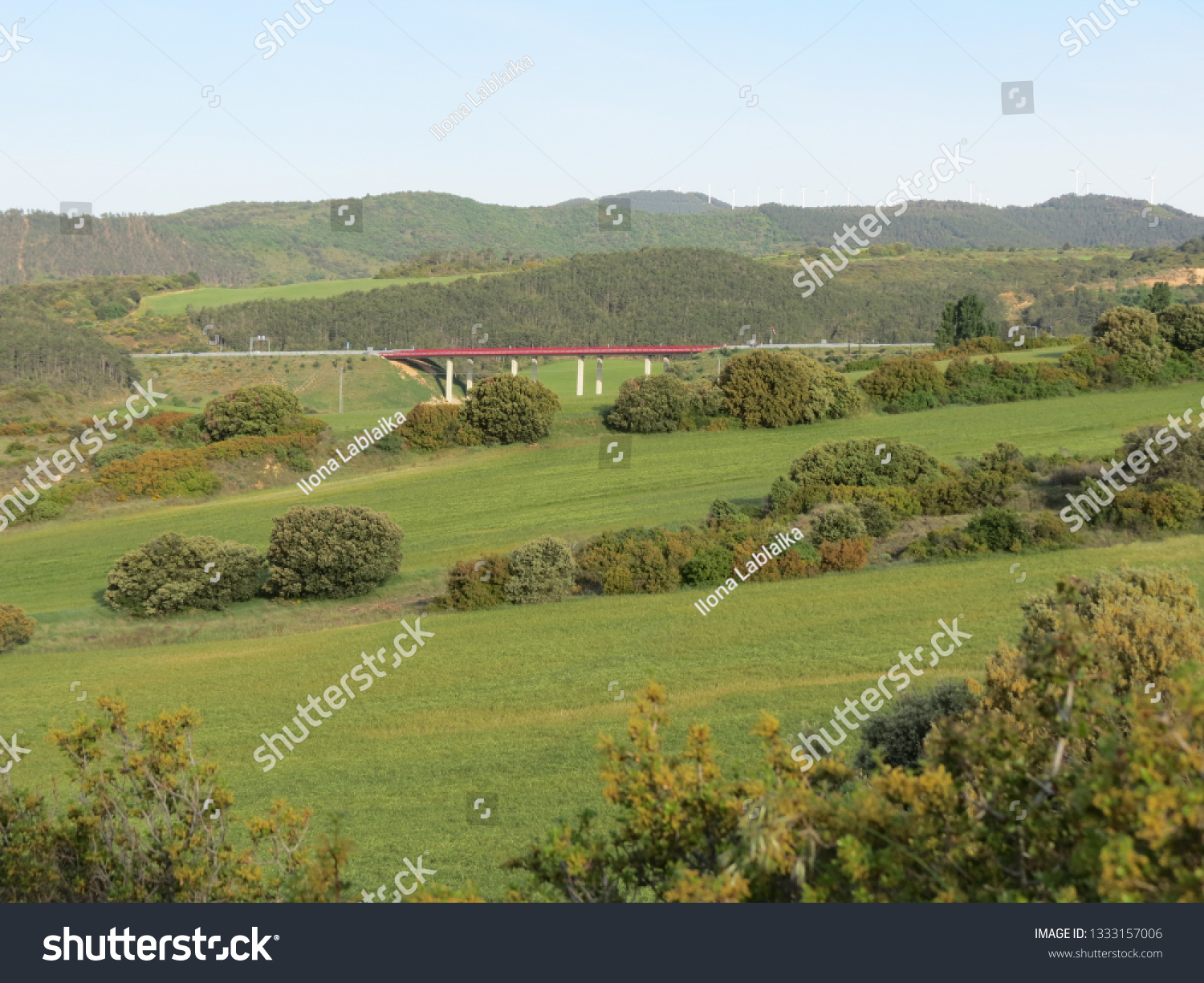 Panoramic Navarra (Spain) landscape with green meadows and modern red bridge in the distance #1333157006