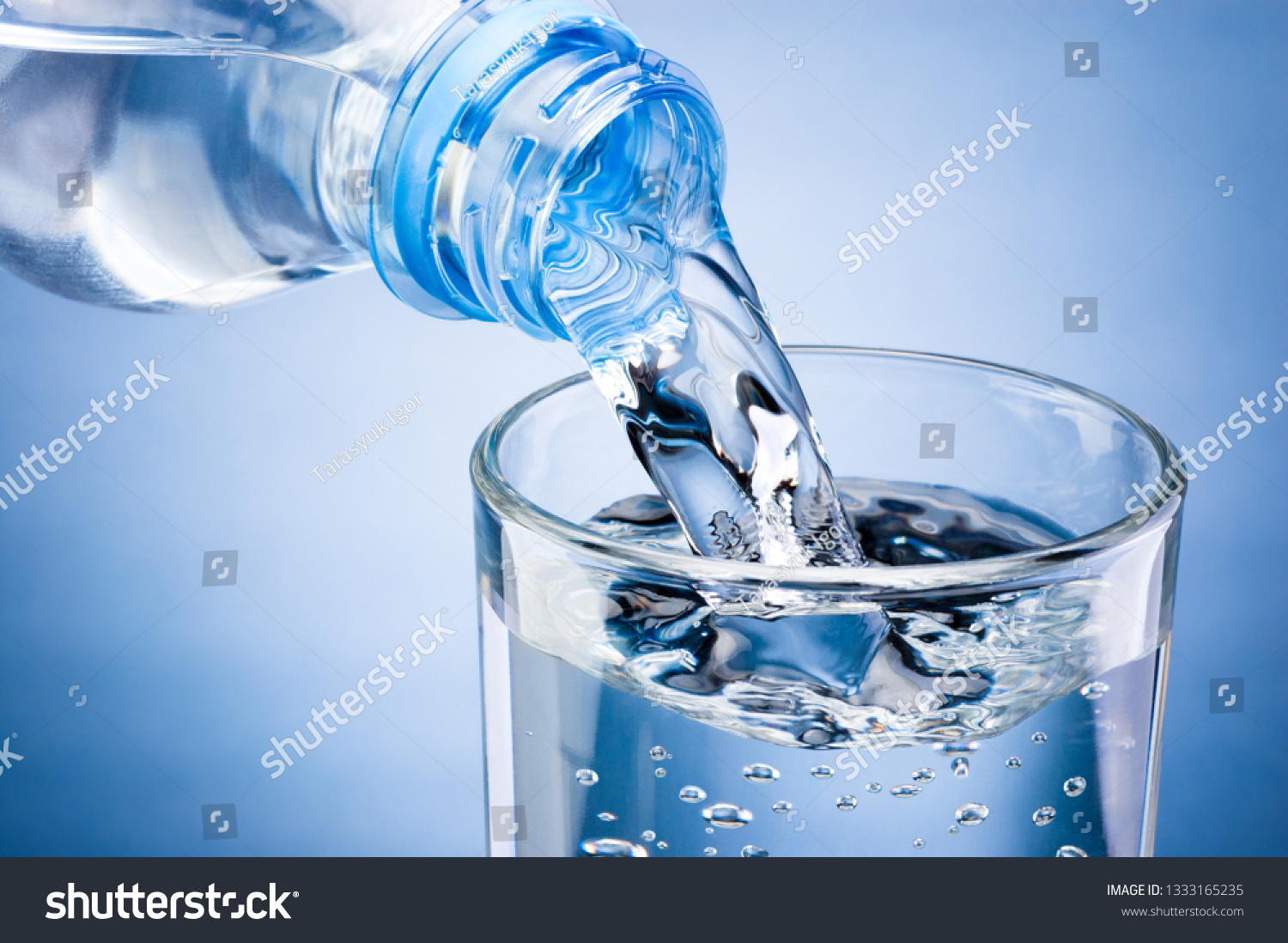 Pouring water from bottle into glass on blue background #1333165235