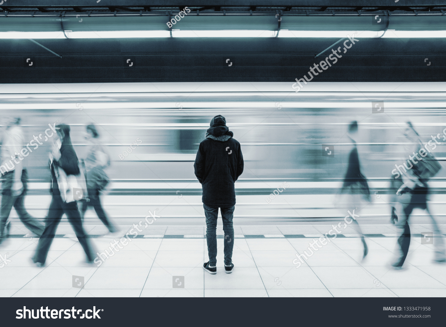Long exposure picture with lonely young man shot from behind at subway station with blurry moving train and walking people in background #1333471958