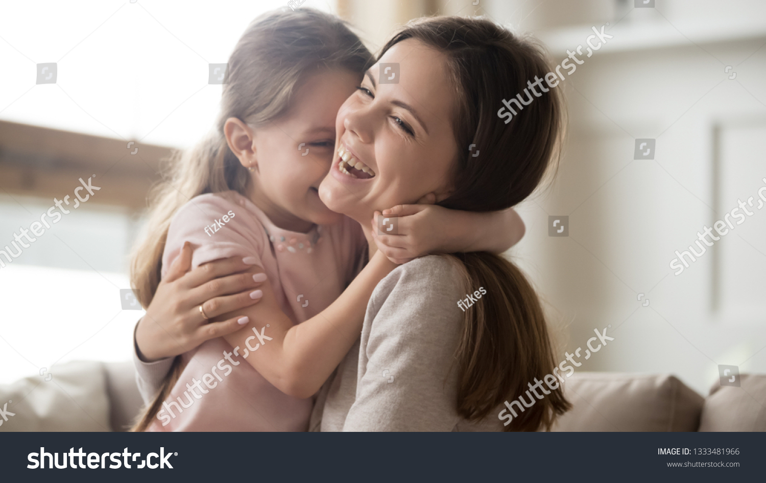 Loving young mother laughing embracing smiling cute funny kid daughter enjoying time together at home, happy family single mom with little child girl having fun playing feel joy cuddling and hugging #1333481966