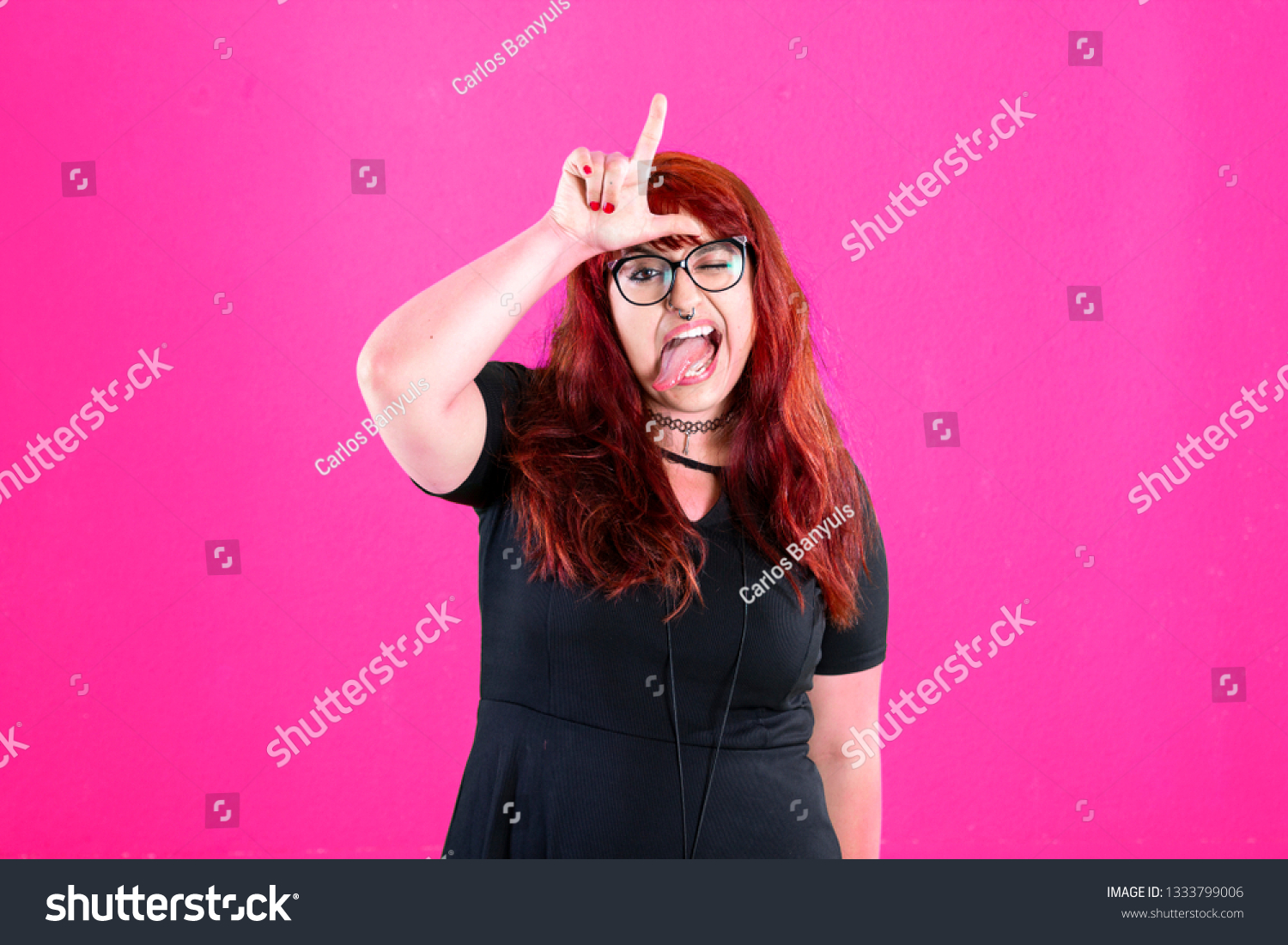 You are outsider. Studio shot of annoyed good-looking woman, feeling cool and confident while tilting head and showing loser-sign over forehead #1333799006