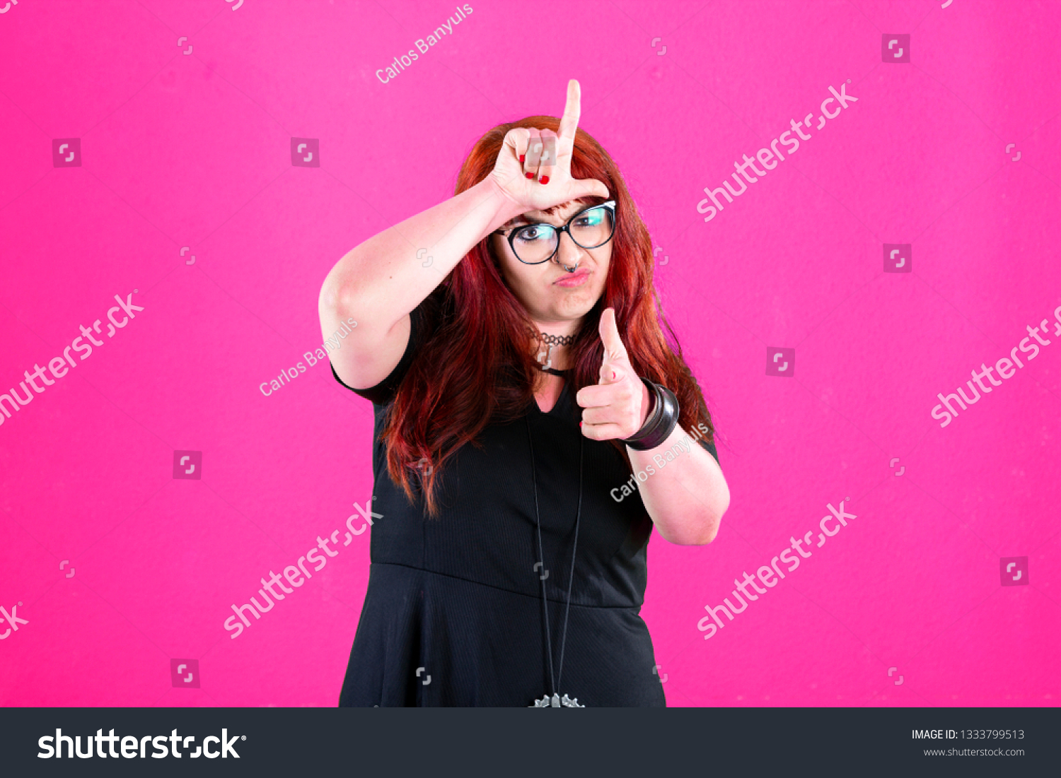 You are outsider. Studio shot of annoyed good-looking woman, feeling cool and confident while tilting head and showing loser-sign over forehead #1333799513