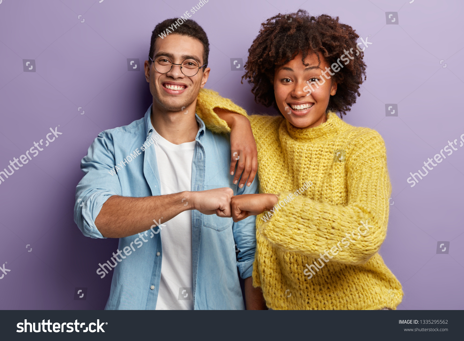 Young diverse couple give fist bump, agree to bring plan to life, smile broadly, have mixed race relationships, have good friendly partners, isolated over purple wall. I agree with you concept #1335295562