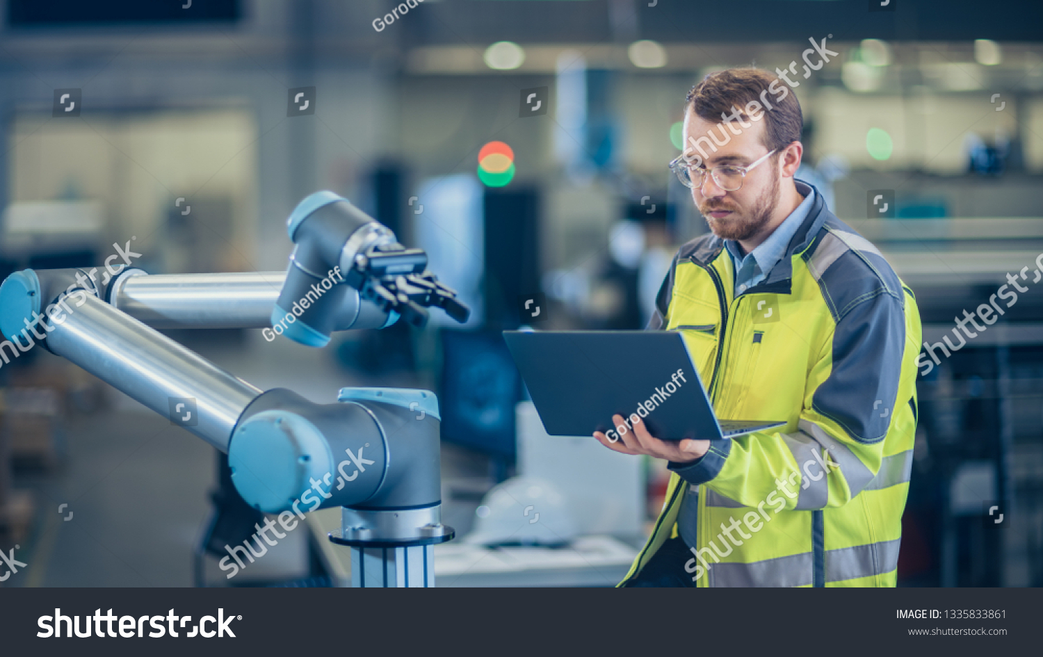 At the Factory: Automation Engineer Uses Laptop for Programming Robotic Arm. New Era in Automatic Manufacturing Industry. #1335833861