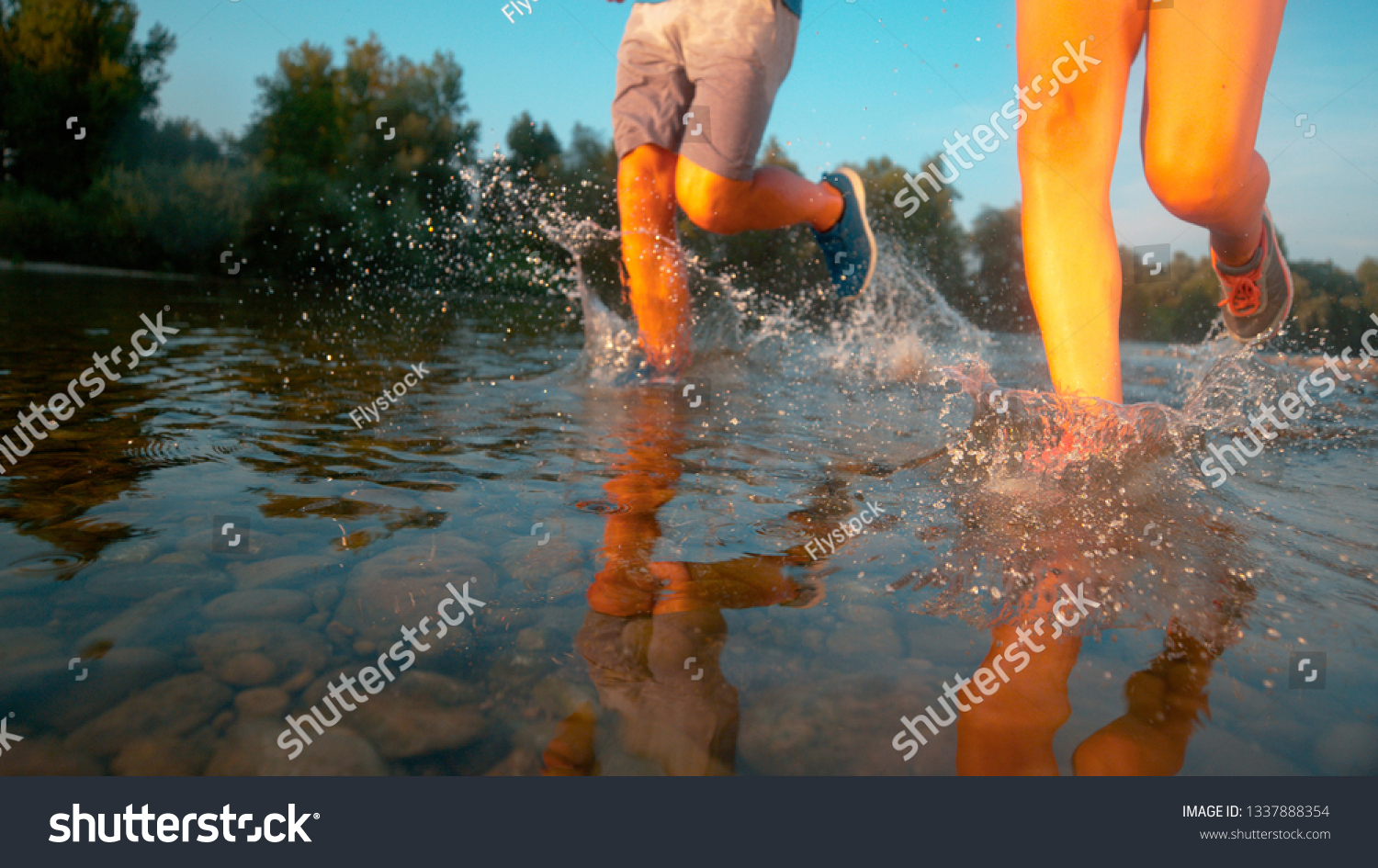 LOW ANGLE: Unrecognizable couple jogging in the shallows of a tranquil river. Fit training partners going for a relaxing jog through the scenic forest and along the refreshing stream. Fun activity #1337888354
