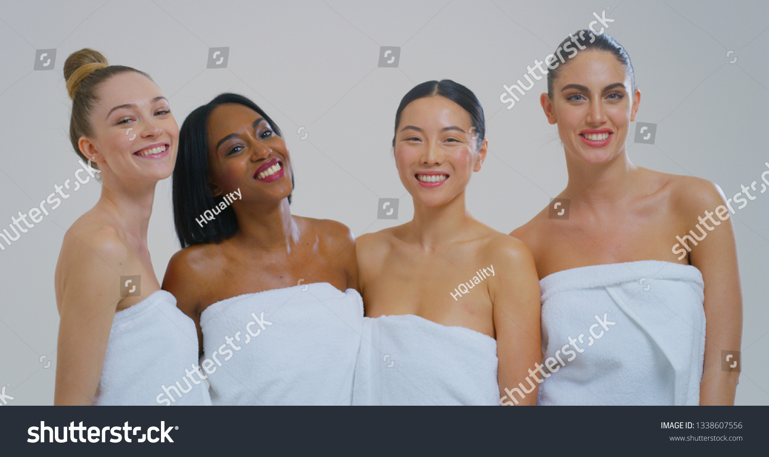 Portrait of beautiful young smiling women of different ethnicities with perfect firm and slim body in white bathing towels isolated on white background. #1338607556