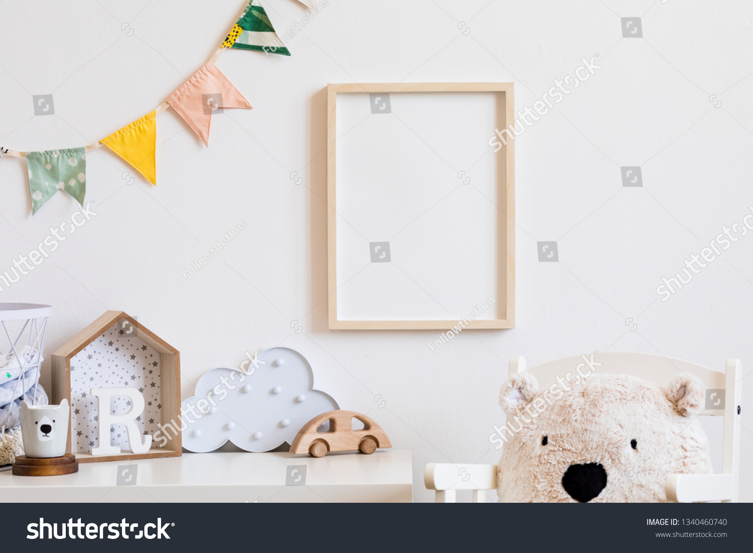 Stylish scandinavian child room with mock up photo poster frame on the white wall. Cute modern interior of nursery with boxes, teddy bear, toys.  wooden accessories and colorful flags. Real photo. #1340460740