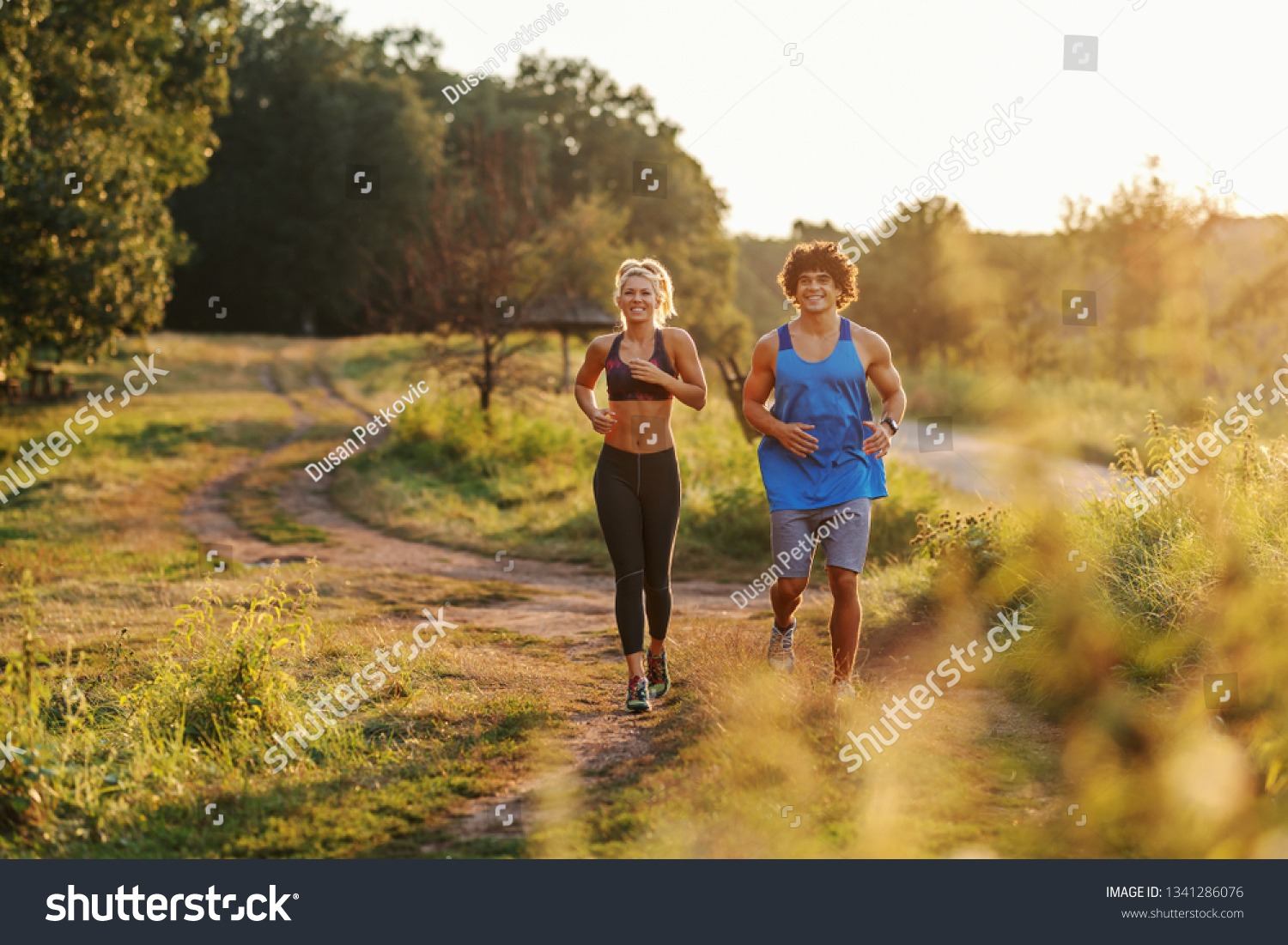 Happy Caucasian couple in sportswear with healthy habits running in nature. Sunny summer day. #1341286076