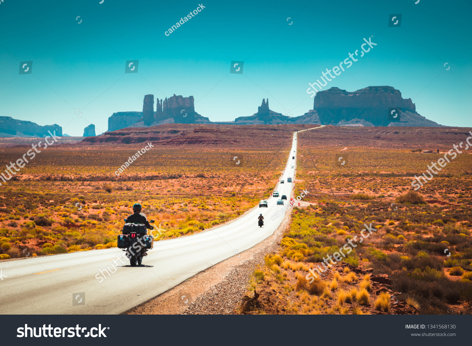 Classic panorama view of motorcyclist on historic U.S. Route 163 running through famous Monument Valley in beautiful golden evening light at sunset in summer, Utah, USA #1341568130