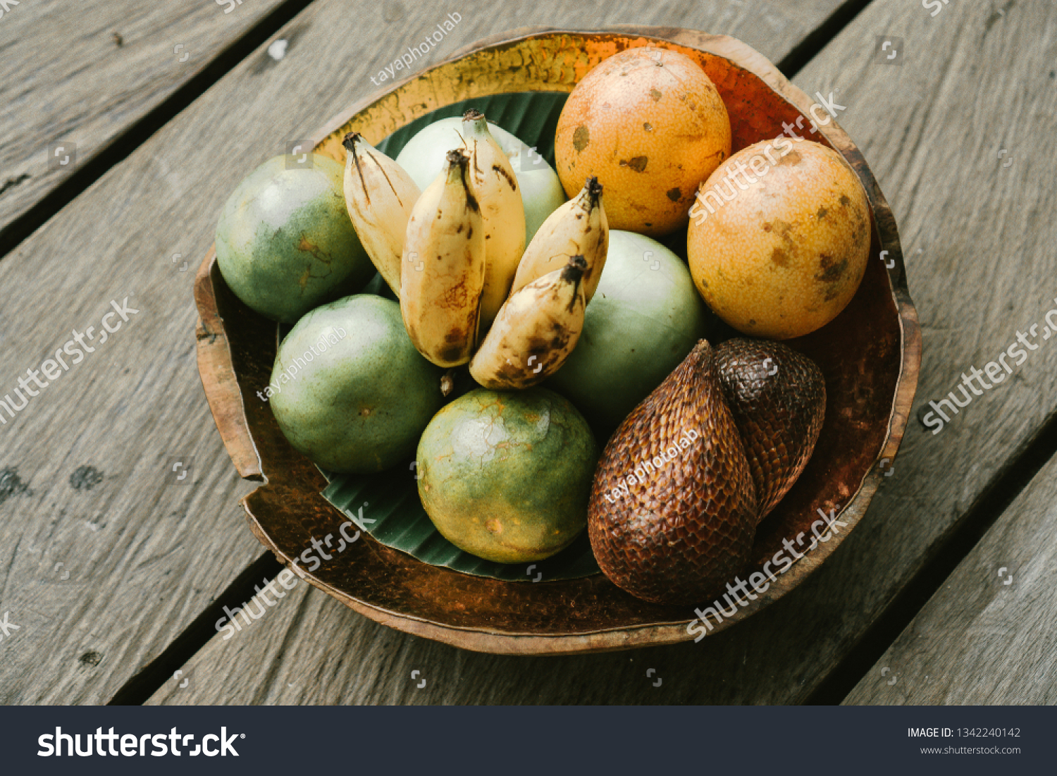 Organic tropical fruits in a platter: snake fruit, passion fruit, bananas. Assorted exotic fruit plate located on a wooden rustic background. Top view. Vegan detox healthy concept. Selective focus.  #1342240142