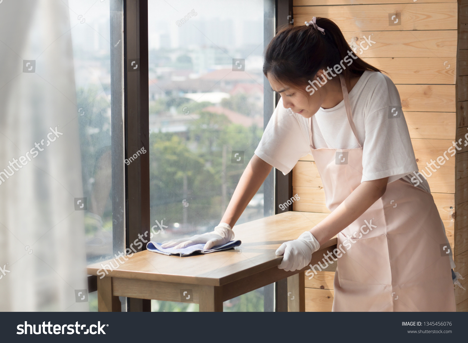 woman cleaner cleaning, disinfecting with disinfectant living room in apartment. portrait of asian woman cleaning staff doing housekeeping or domestic helper job. young adult asian woman model #1345456076
