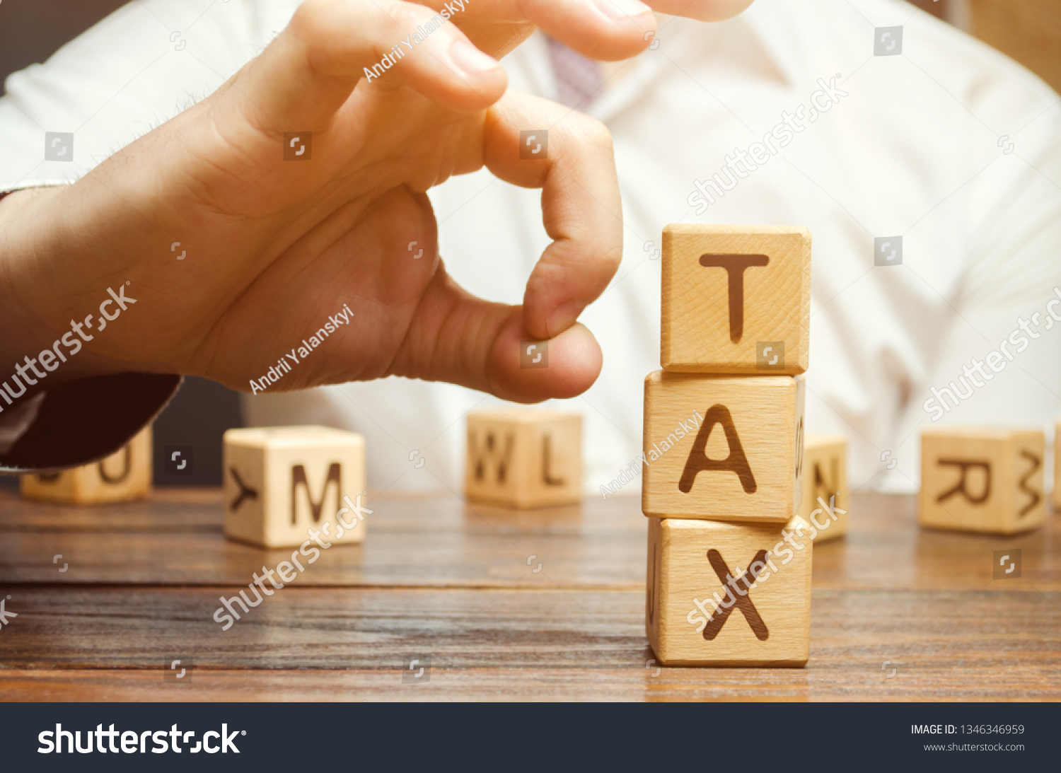 Businessman removes wooden blocks with the word Tax. The concept of reducing the tax burden. Tax avoidance. Costs and expenses of the business. Taxation. Pay off debt. Freedom from illegal taxes #1346346959