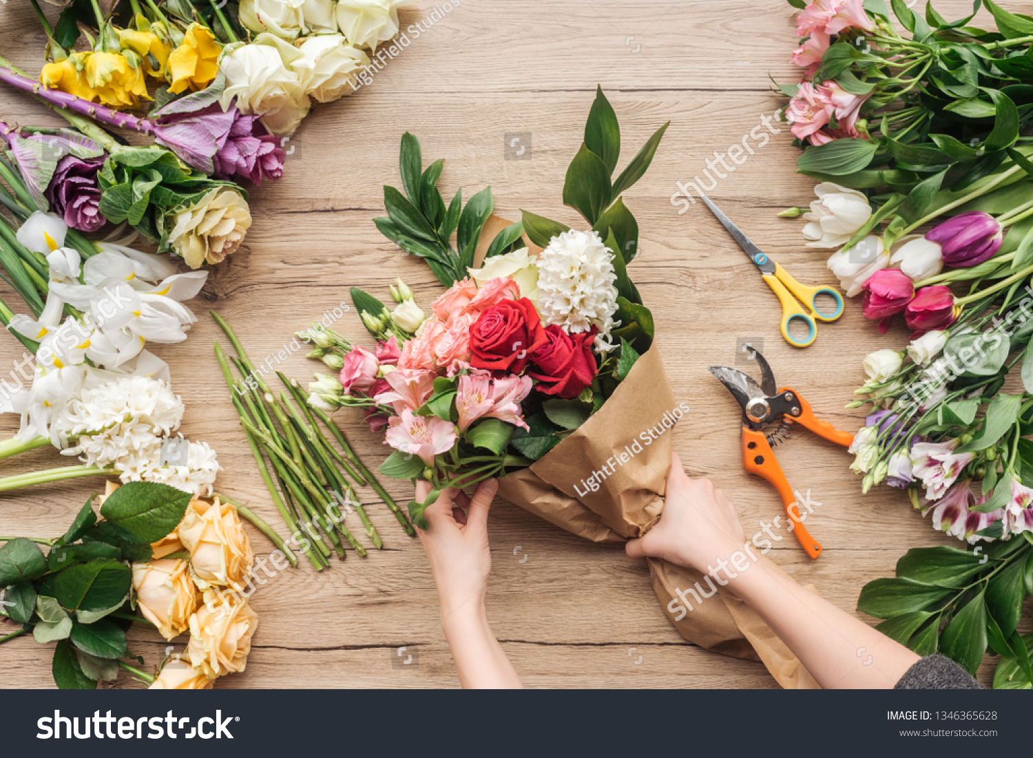 Cropped view of florist making flower bouquet on wooden surface #1346365628