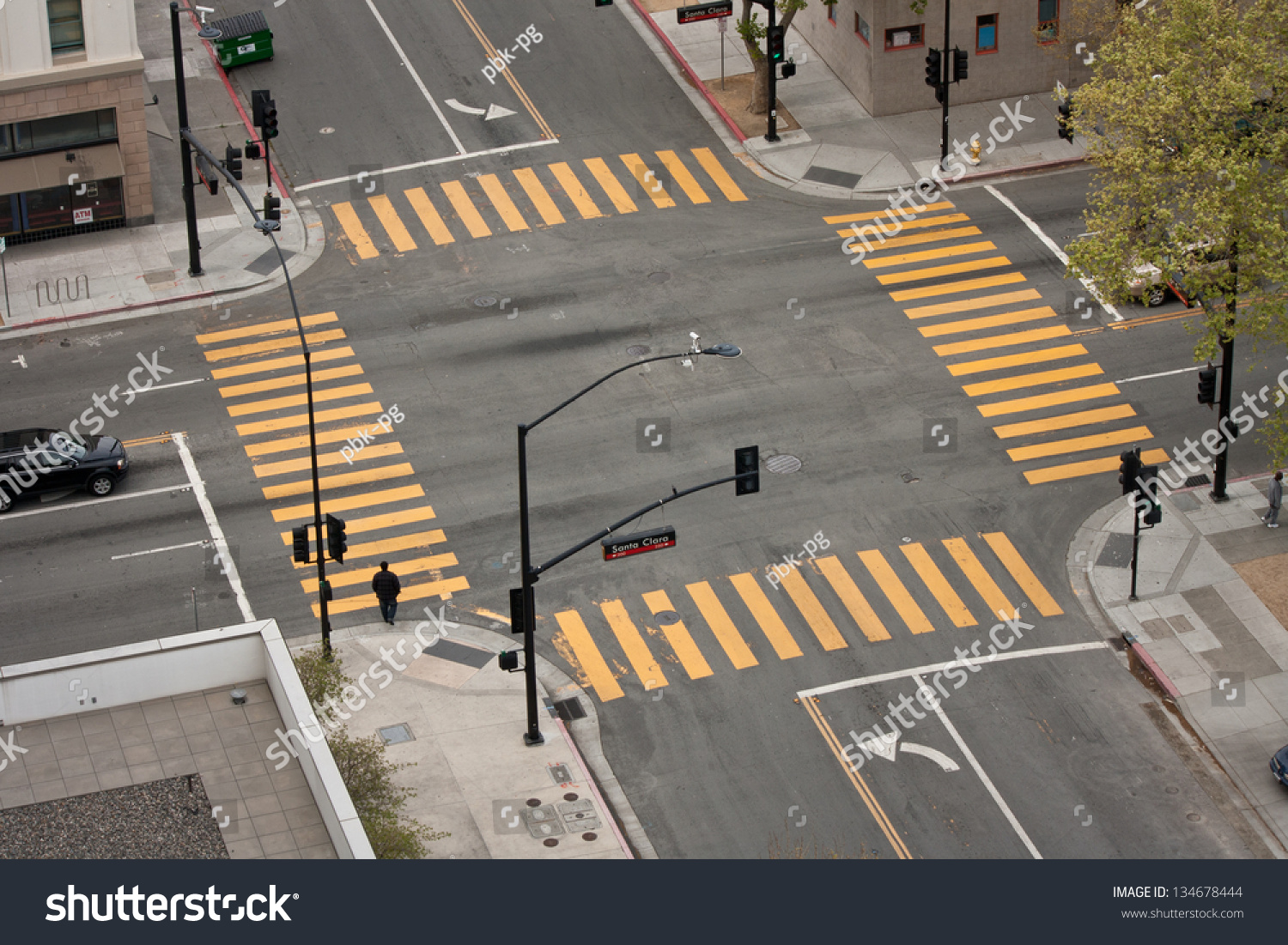 A high angle view of an almost empty street intersection, with yellow cross walk markings, traffic signal lights, and curb cuts, in San Jose, California. #134678444