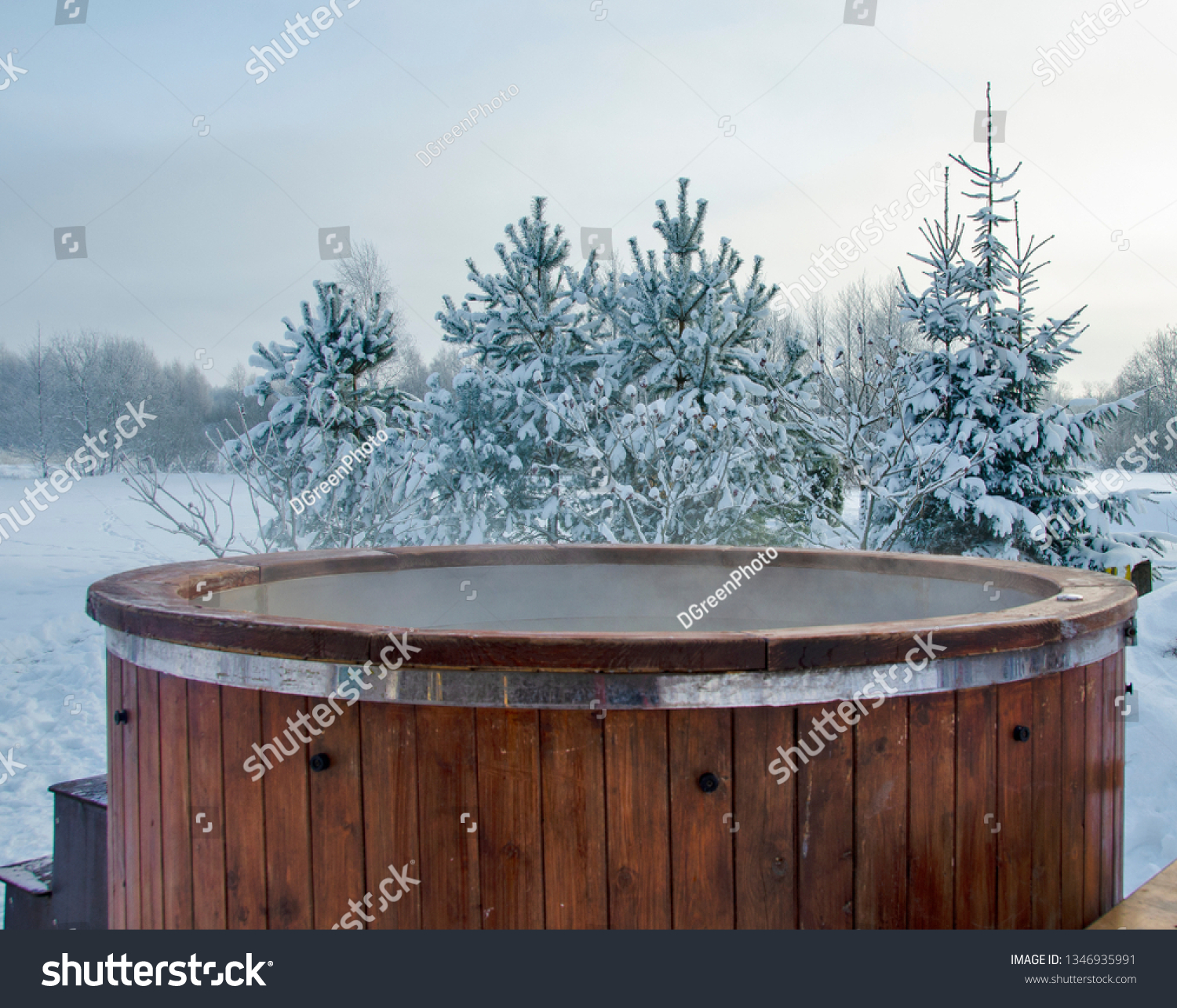 Steaming wooden hot tub with spa in winder with  snow and frosty Christmas trees in background - Image #1346935991