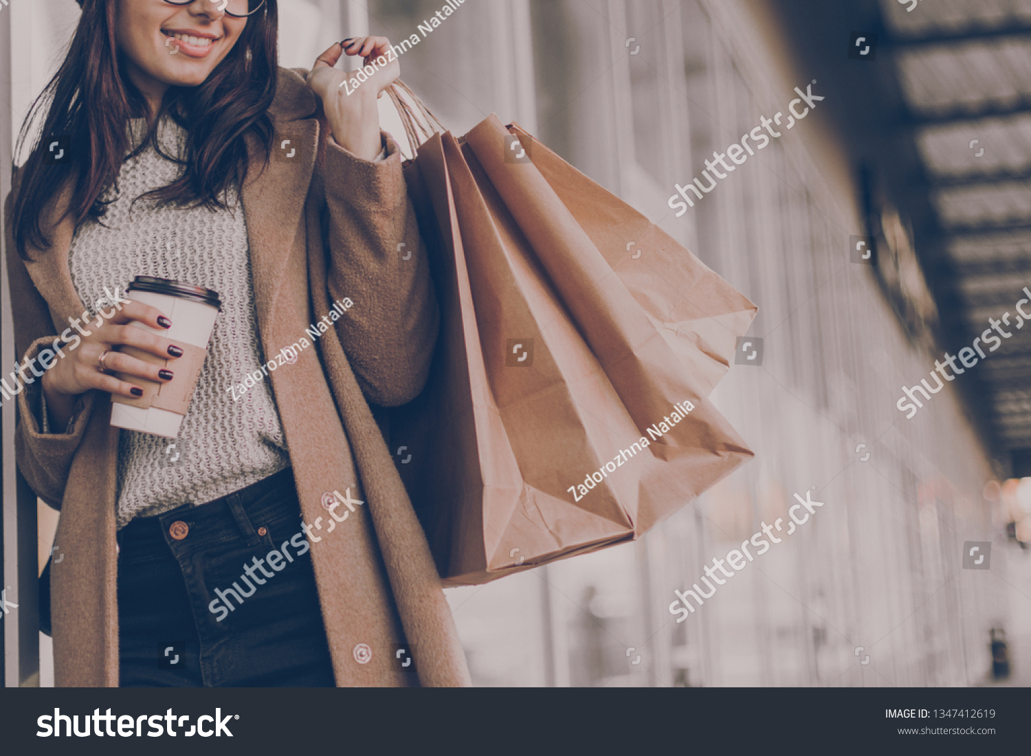 Beautiful fashionable woman drink coffee walking near mall with shopping bags. #1347412619