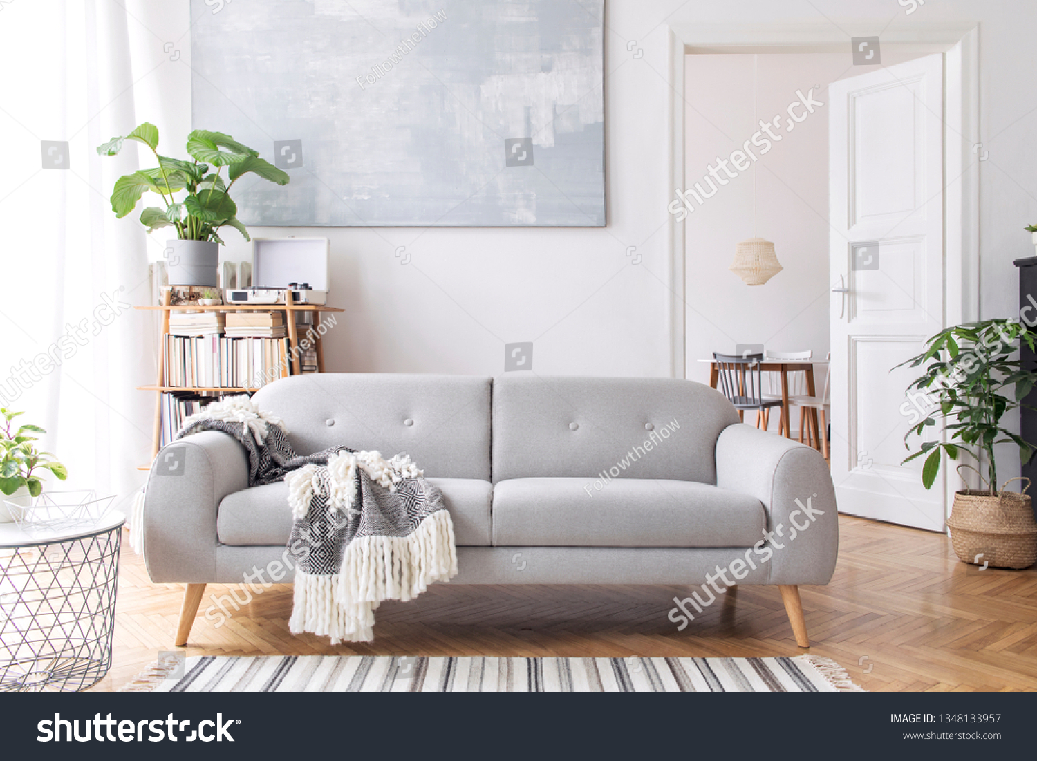 Stylish scandianvian living room with design sofa with elegant blanket, coffee table and bookstand on the white wall. Brown wooden parquet. Concept of minimalistic decor interior with piano. Mock up. #1348133957