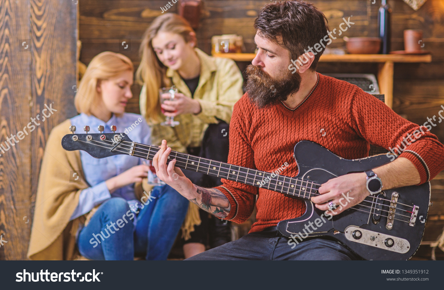 Girls listening to song performed by handsome bearded musician. Guitarist entertaining guests at party. Man with hipster beard playing electrical guitar. Bearded man united with his instrument. #1349351912