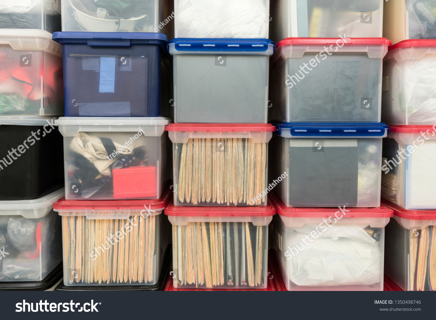 Stacked plastic file storage boxes with folders, binders and miscellaneous items.   #1350498746
