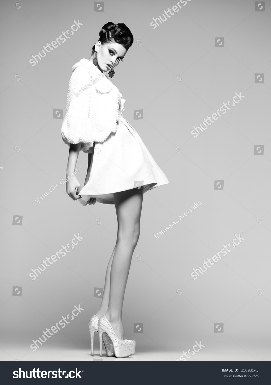 beautiful woman with long legs in white dress, fur and high-heels posing in the studio #135098543