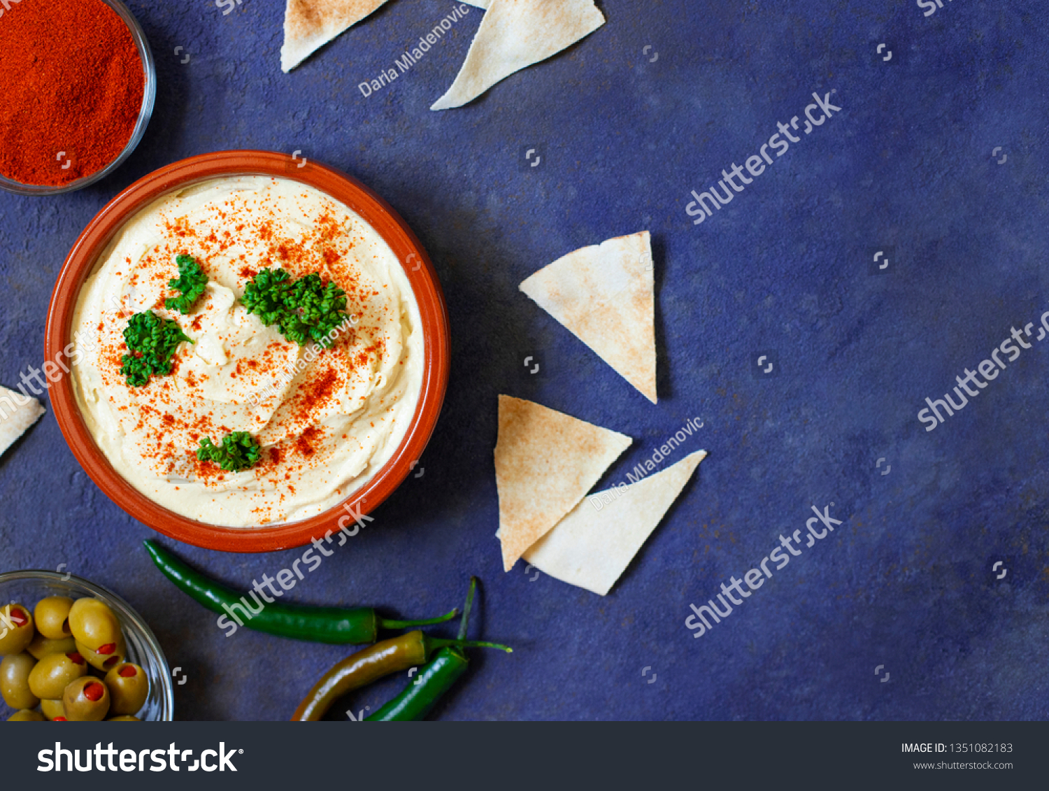 Healthy homemade hummus served with paprika powder, pita bread, olives and parsley. Middle Eastern cuisine, Israeli cuisine, Levanese cuisine, Levantine cuisine. Dark background. Top view #1351082183