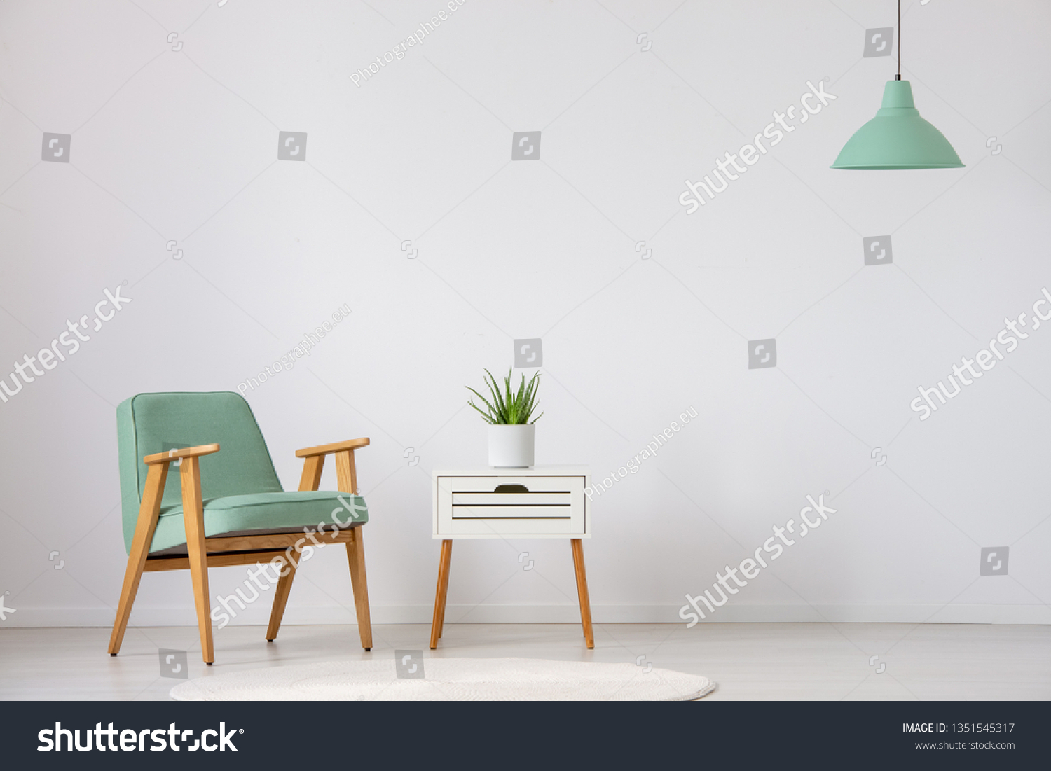 Vintage mint armchair next to small white table with green plant in pot in bright interior, real photo with copy space on the empty wall #1351545317