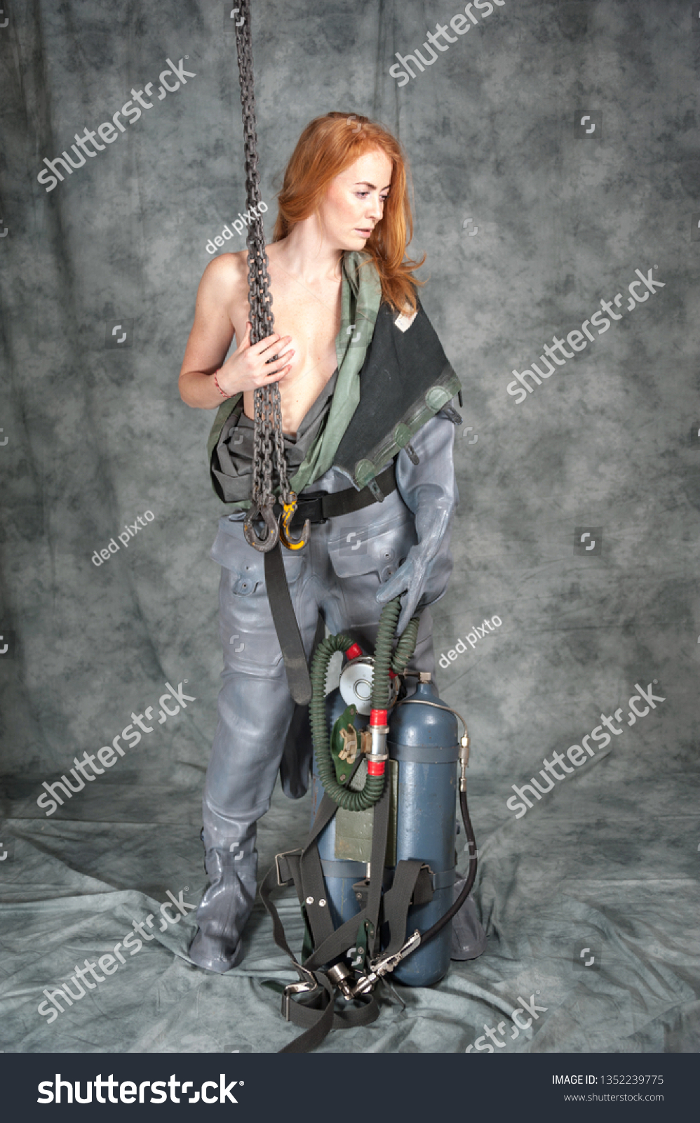 Nude young woman with red hair and freckles with a chain in her hands in a vintage diving suit. #1352239775