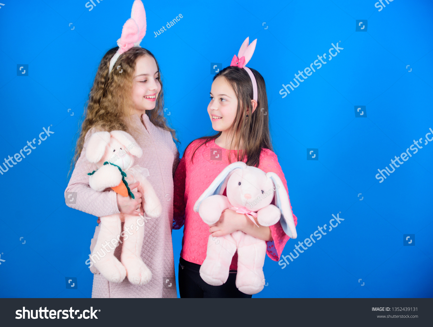 Children with bunny toys on blue background. Sisters smiling cute bunny costumes. Spread joy and happiness around. Friends little girls with bunny ears celebrate Easter. Hope love and joyful living. #1352439131
