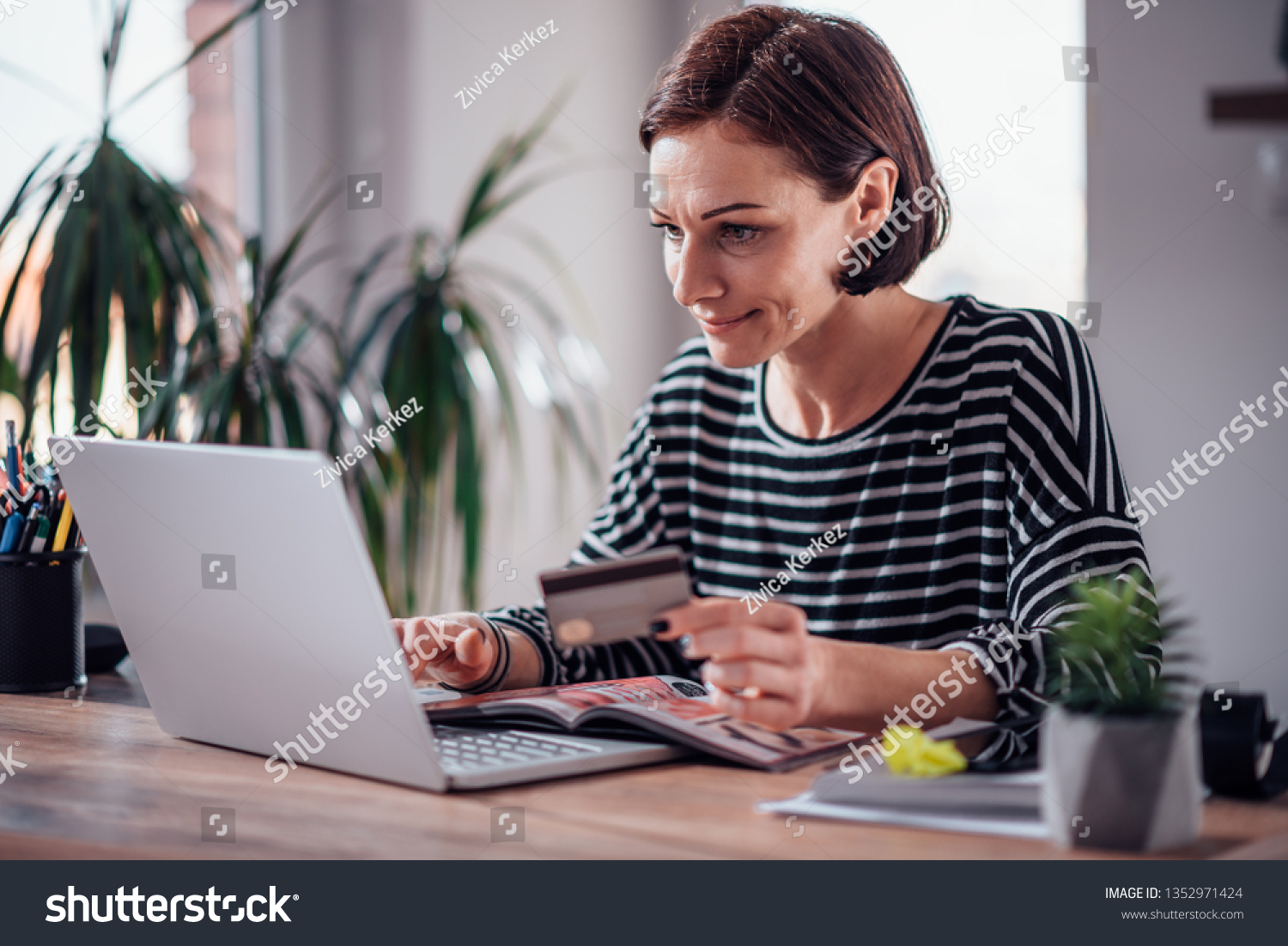 Woman shopping online and using credit card while reading cosmetic catalogue #1352971424