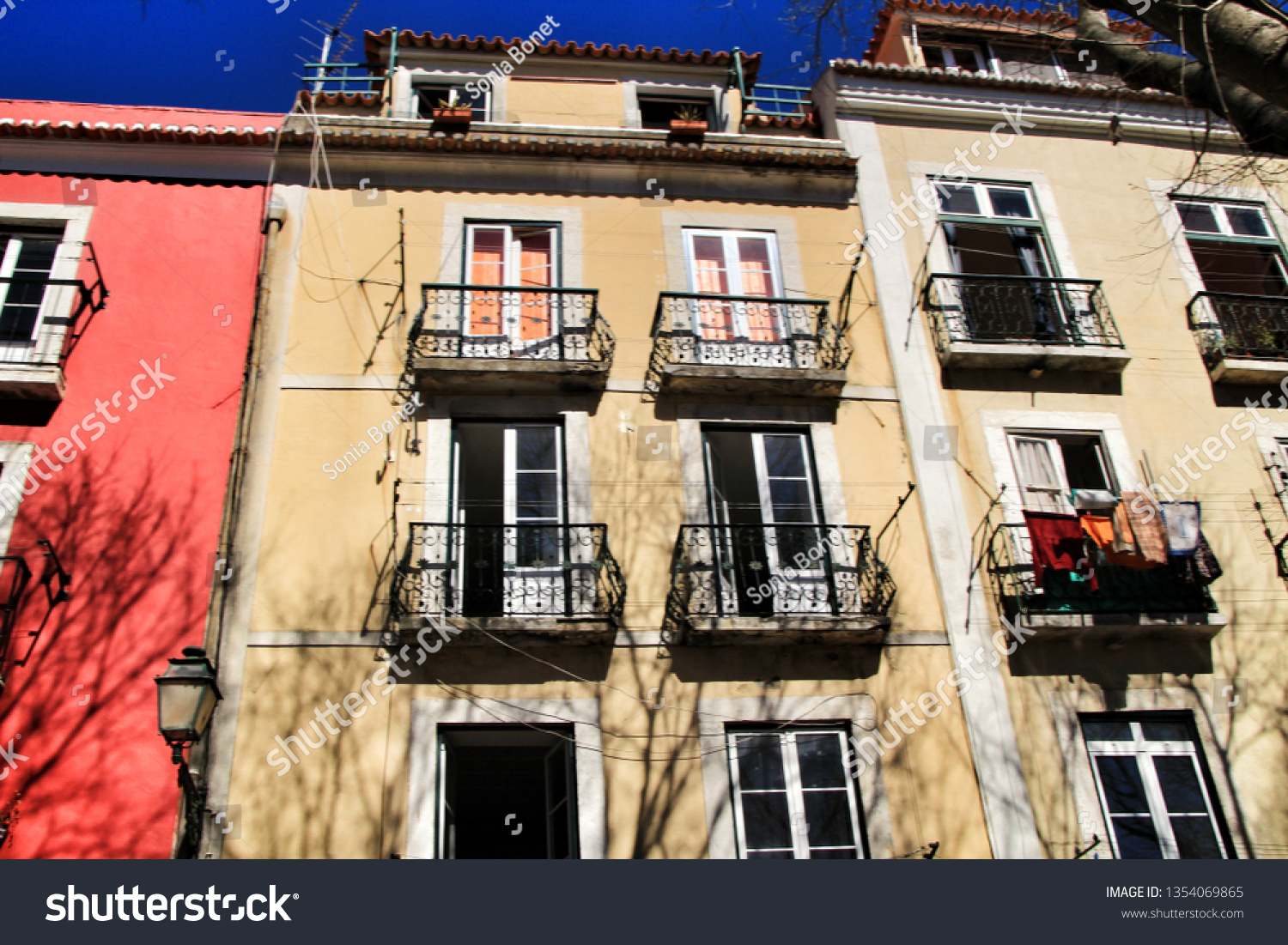 Old colorful and beautiful facades with vintage streetlight in Lisbon streets in Spring. Clothesline in the facade with hanging clothes #1354069865
