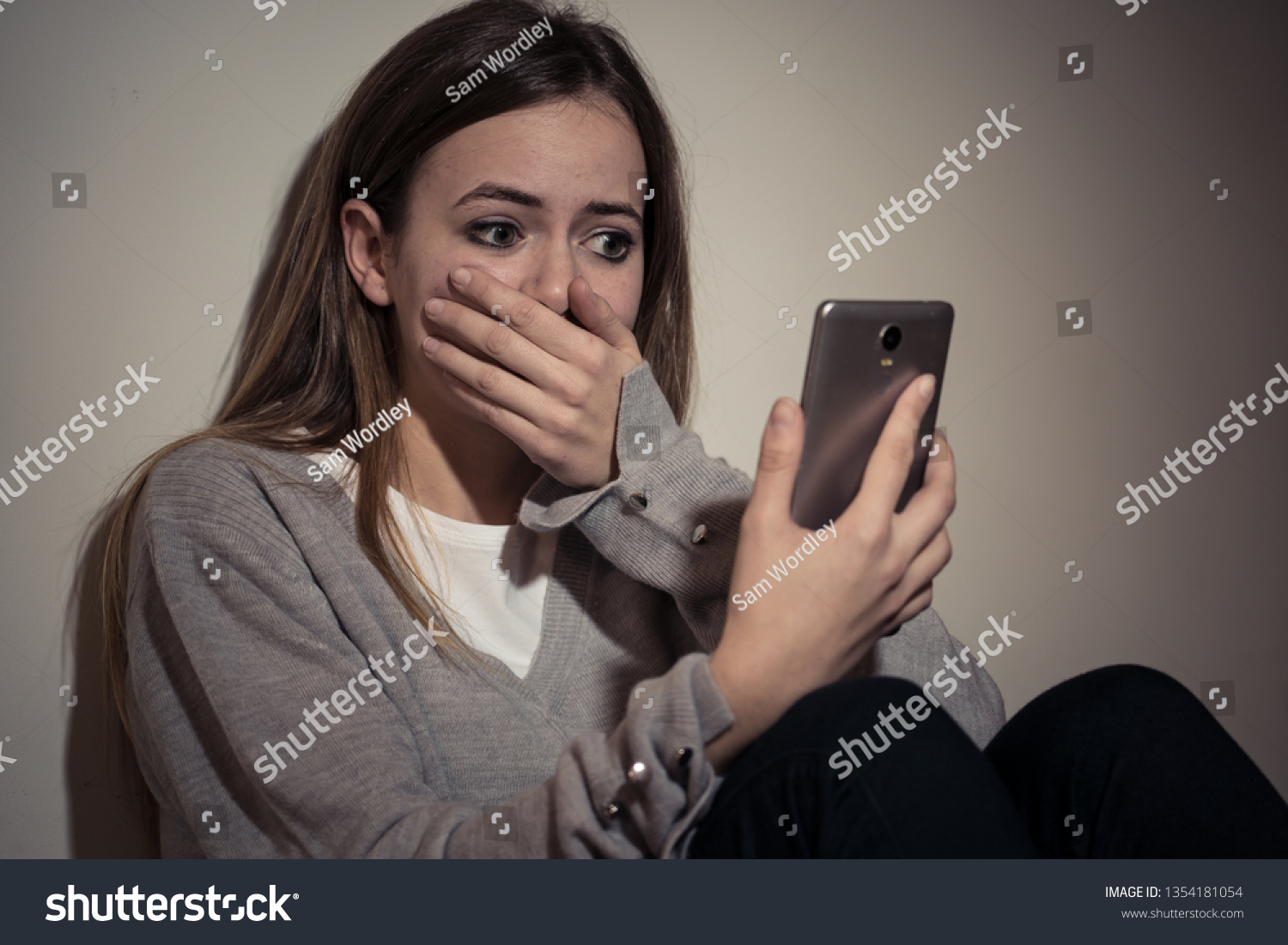 Sad desperate young teenager female girl on smart phone suffering from online bulling and harassment felling lonely and hopeless sitting on bed at night. CYberbullying and dangers of internet concept. #1354181054