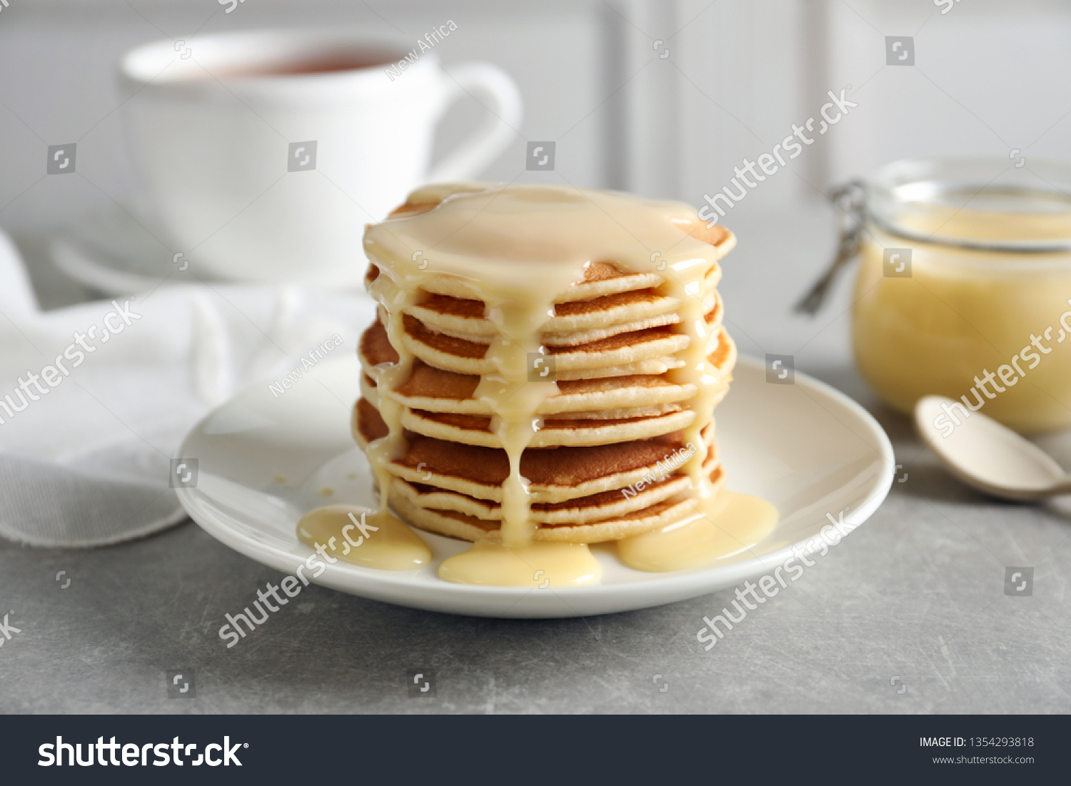 Plate with pancakes and condensed milk served on table. Dairy product #1354293818