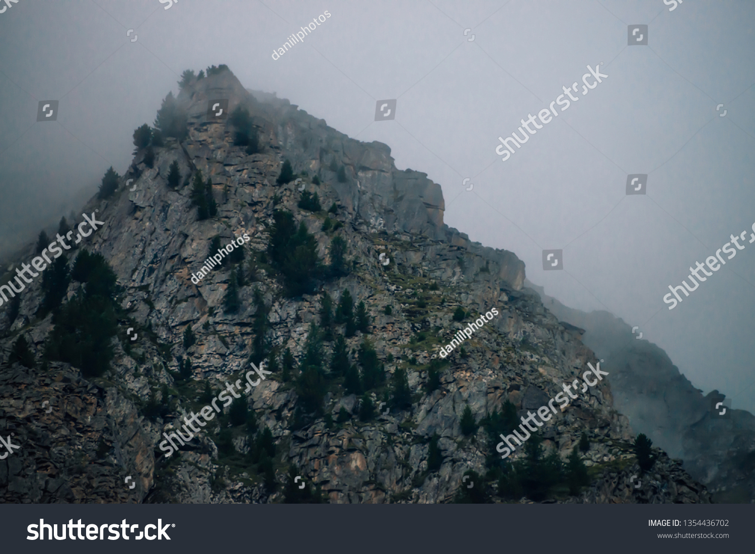 Ghostly giant rocks with trees in thick fog. Mysterious huge mountain in mist. Early morning in mountains. Impenetrable fog. Dark atmospheric eerie landscape. Tranquil mystic atmosphere of wilderness. #1354436702